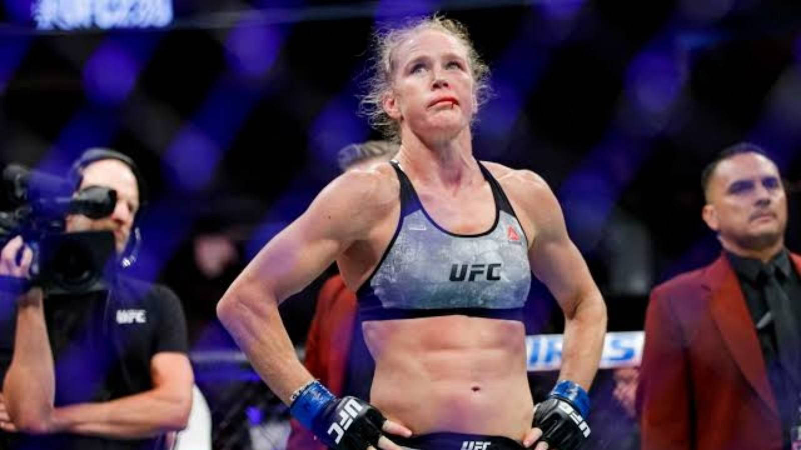 Holly Holm - MMA選手兼前拳擊手 壁紙 — 一位女性UFC拳手在八角籠中勝利站立，在明亮的場館燈光下展現勝利表情。