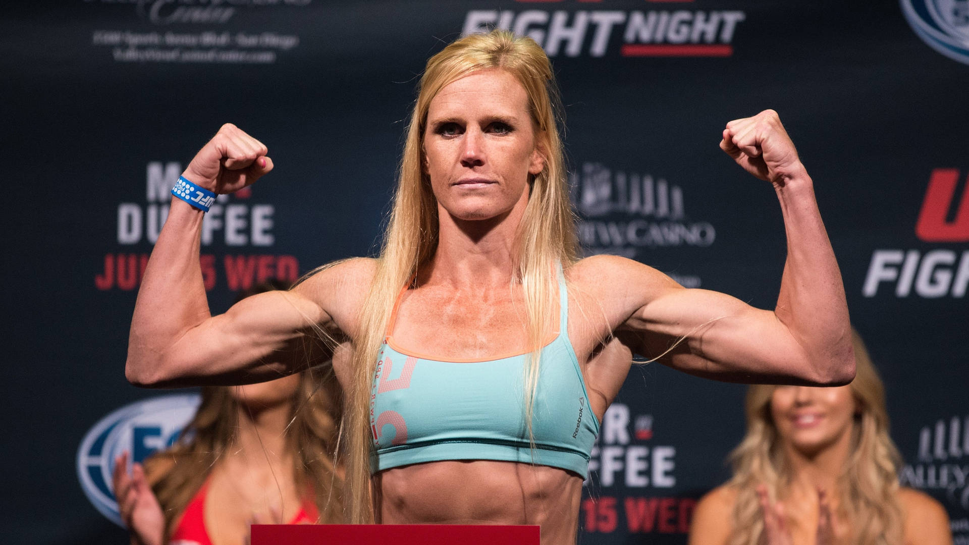 女拳手在稱重活動中彎曲雙臂，帶有 fight night 品牌標誌。 — 淺藍色 壁紙