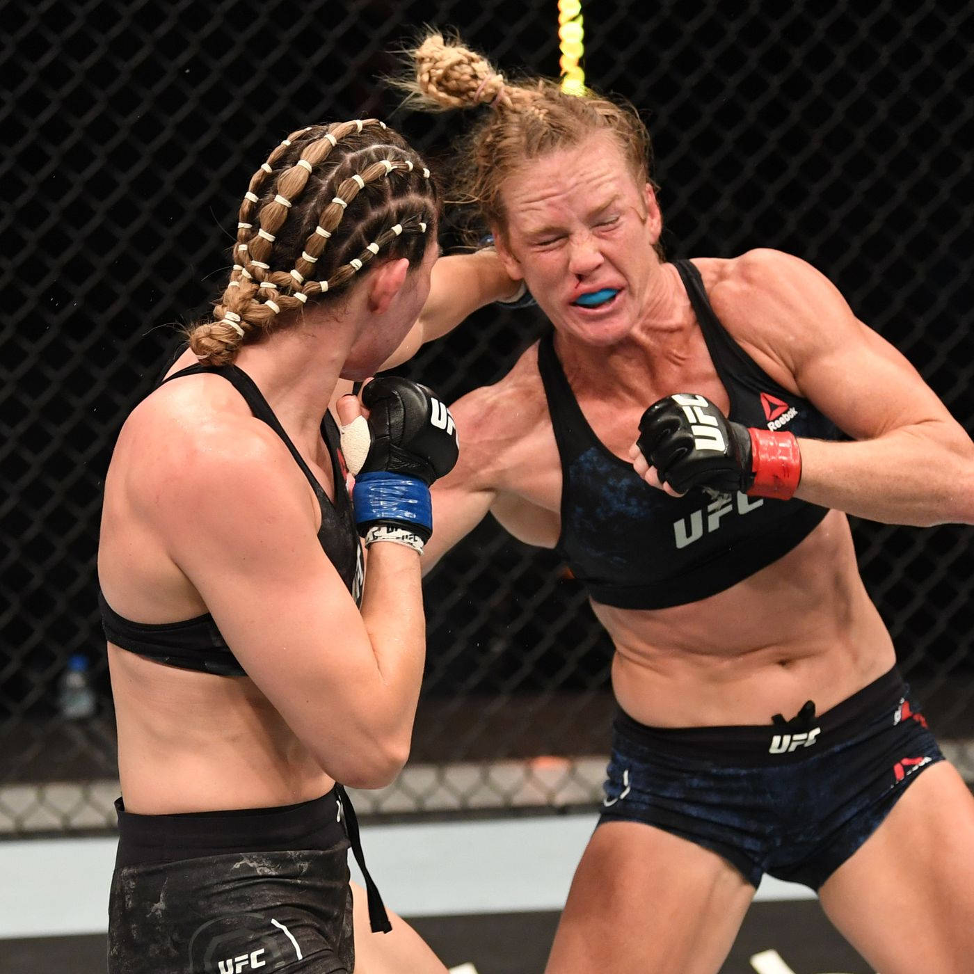 Holly Holm對決Irene Aldana 壁紙 — 兩名女性MMA拳手在激烈的籠中比賽中交鋒，汗水飛濺，表情兇猛。
