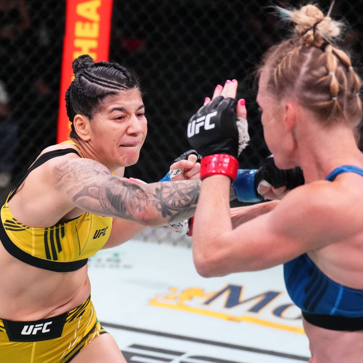 Holly Holm對決Ketlen Vieira 壁紙 — 兩位身穿黃色和藍色裝備的女性UFC拳手在八角籠內擊掌，帶有紋身和專注的表情。