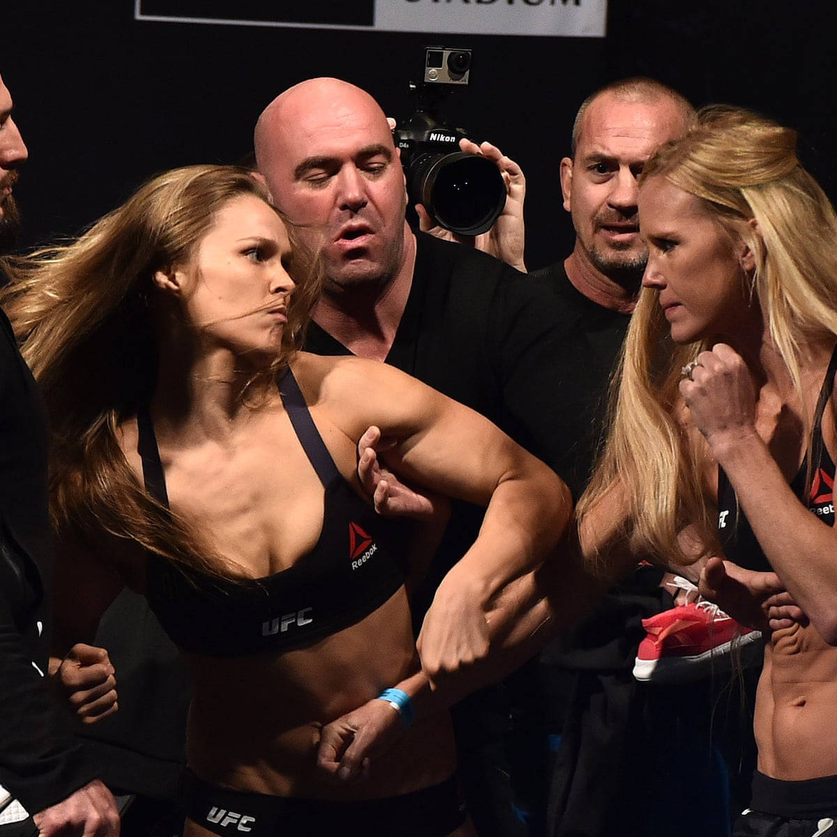 Holly Holm與Ronda Rousey爭執 壁紙 — 兩名女性MMA拳手在官員和攝影師的包圍下，在稱重時激烈對峙。