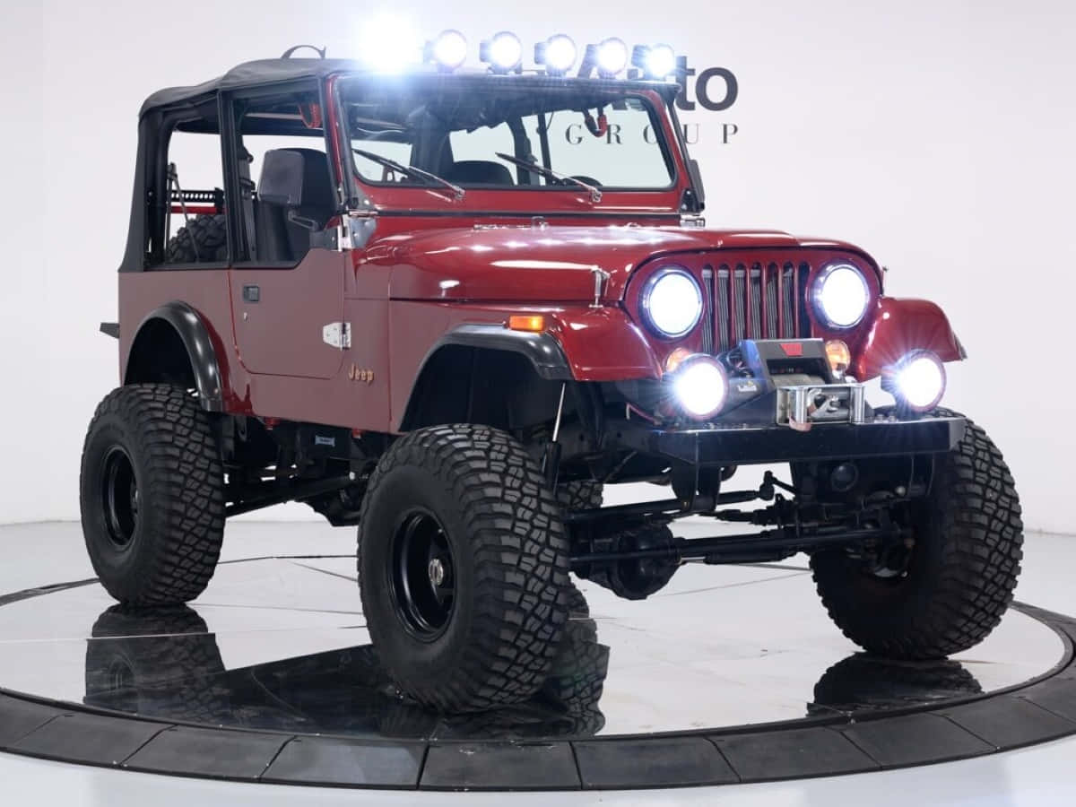 Jeep Cj 桌布 壁紙 — 一輛光澤的紅色經典Jeep Wrangler，配備超大輪胎和明亮頭燈，站立在圓形展廳旋轉台上。