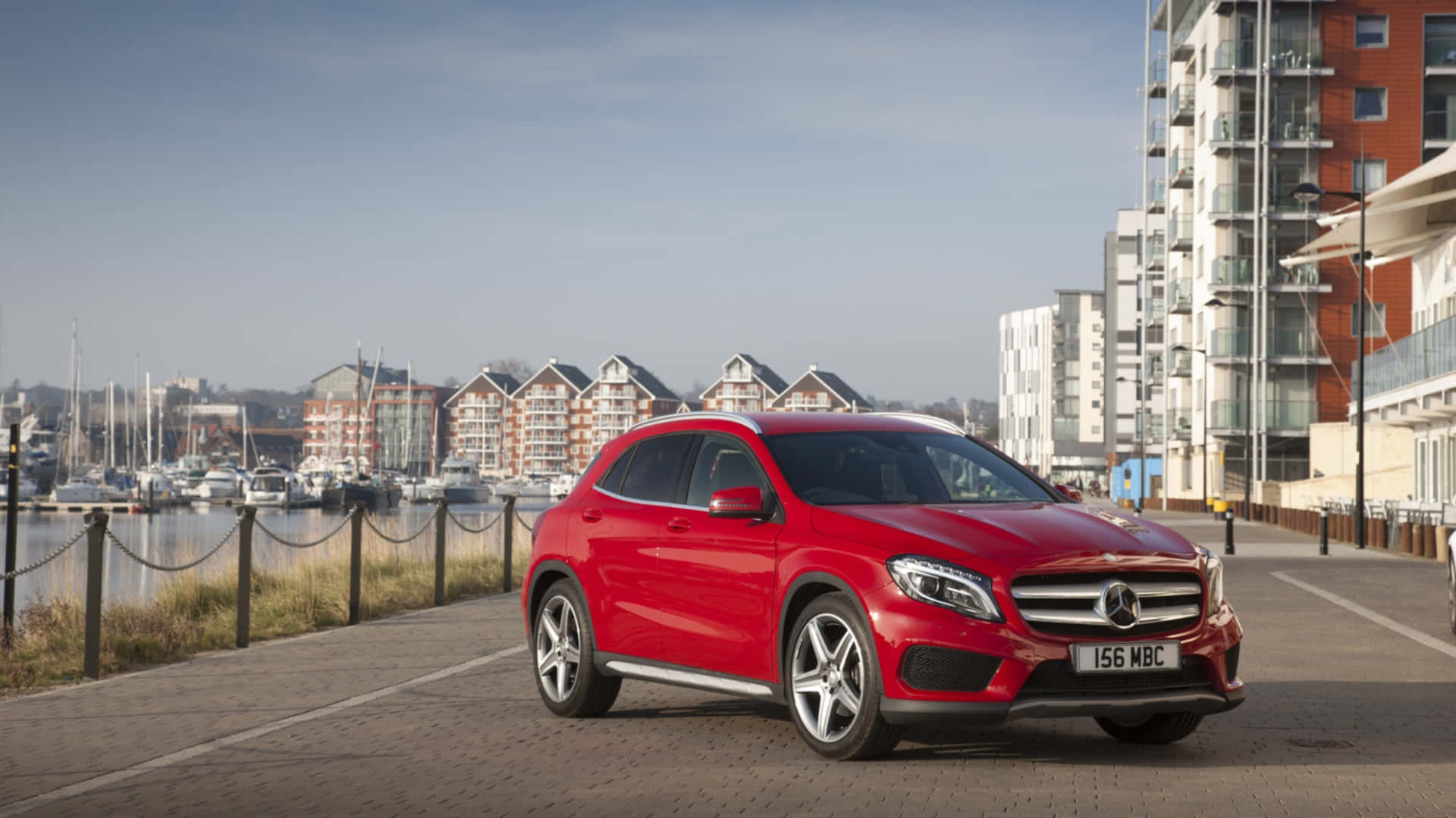 Mercedes Benz Gla-class 桌布 壁紙 — 一架亮紅色Mercedes GLA-Class SUV停在海濱長廊上，背景有現代建築和遊艇碼頭的船隻，天空清澈湛藍。