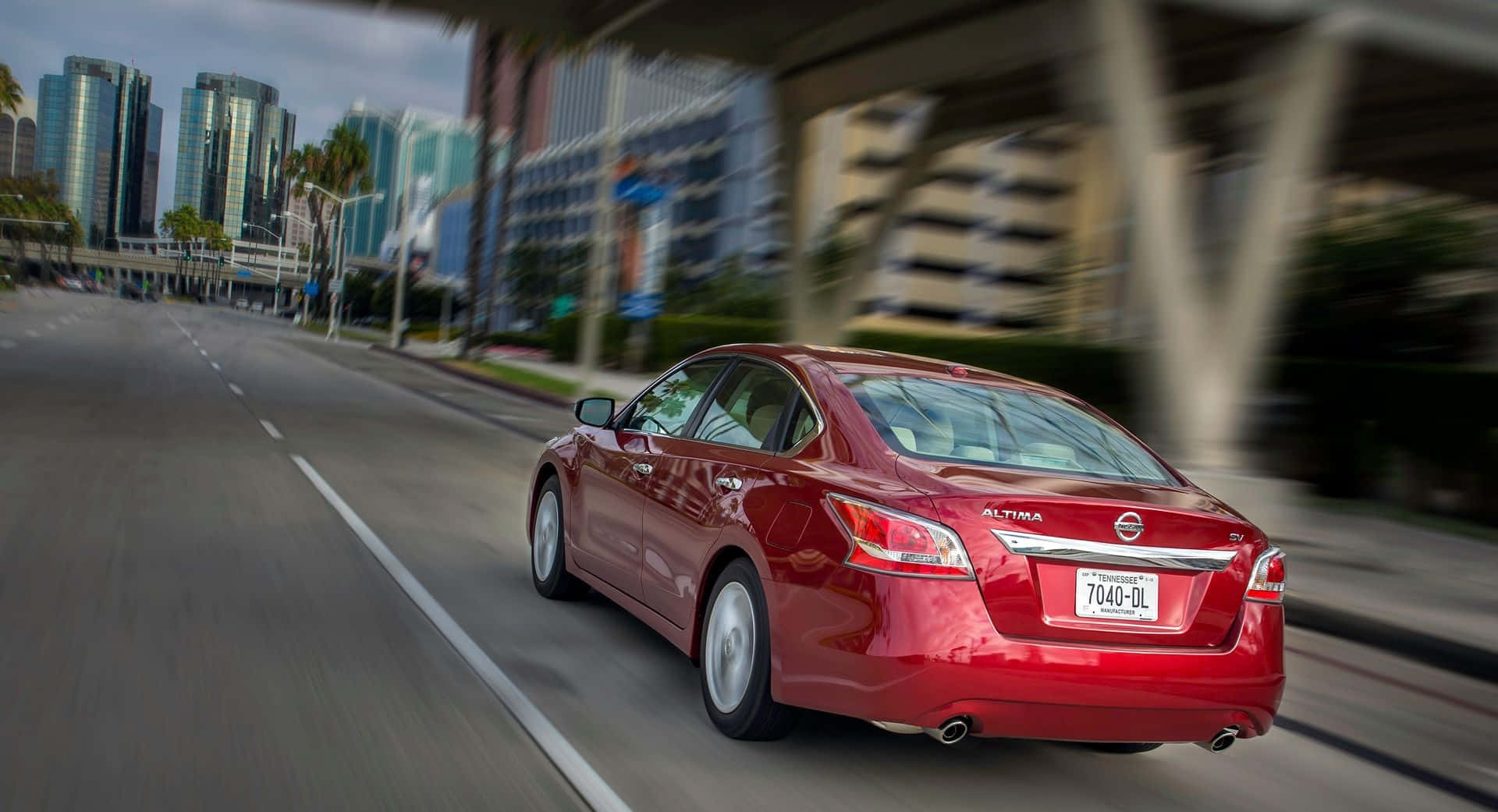 Nissan Altima 桌布 壁紙 — 一輛紅色日產Altima房車在街道上疾馳，背景是模糊的摩天大樓和天橋。