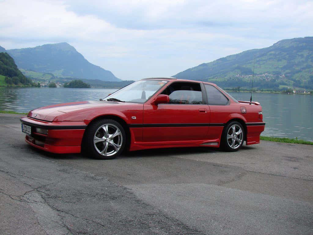 Honda Prelude 桌布 壁紙 — 一架鮮紅色跑車停泊在平靜的湖邊，背景是綠色的山脈，天空多雲。