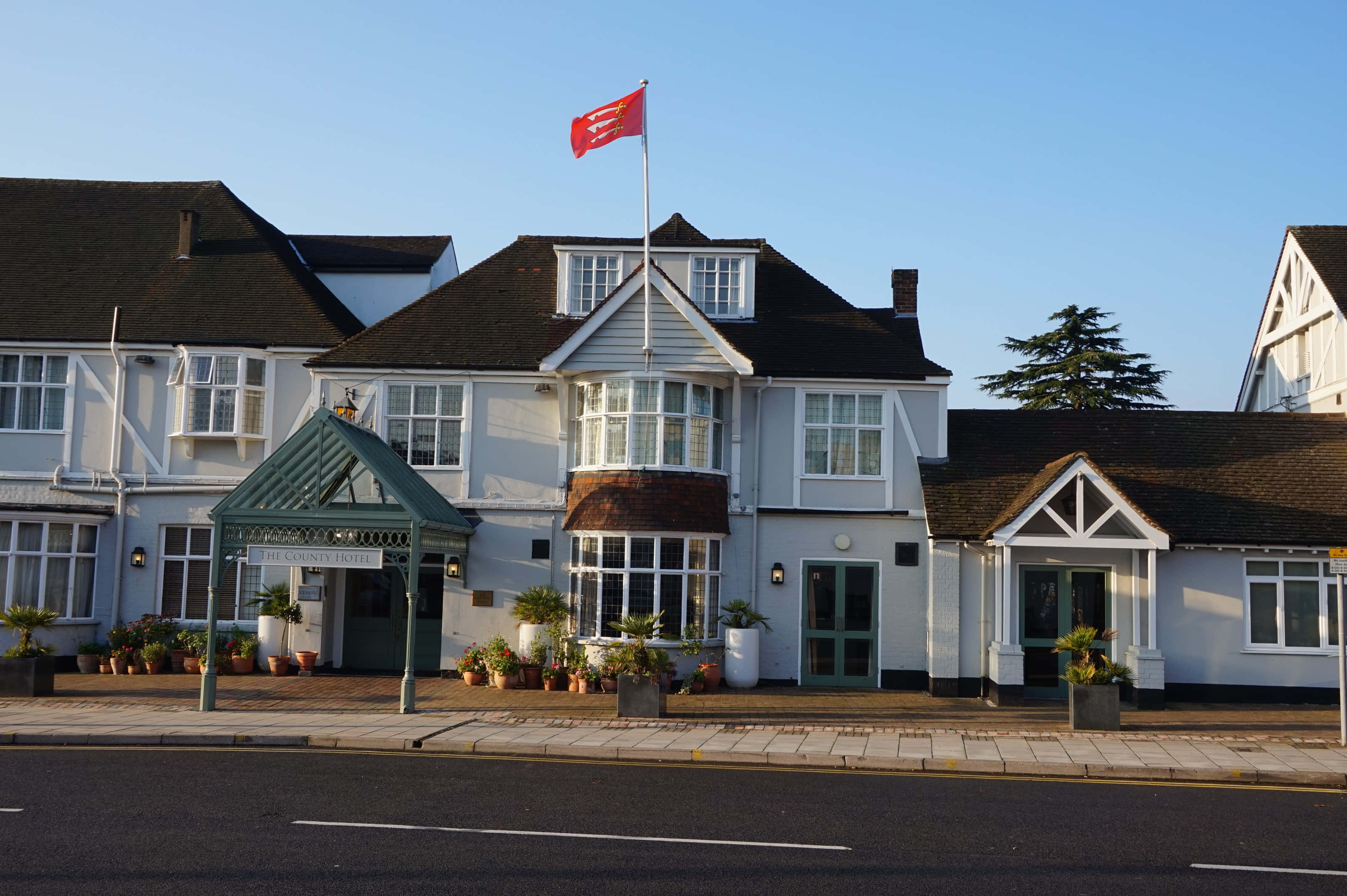 Chelmsford United Kingdom 桌布 壁紙 — 一座宏偉的白色都鐸風格酒店，帶有綠色飾邊，一面紅旗在清澈的藍天下自豪地飄揚。