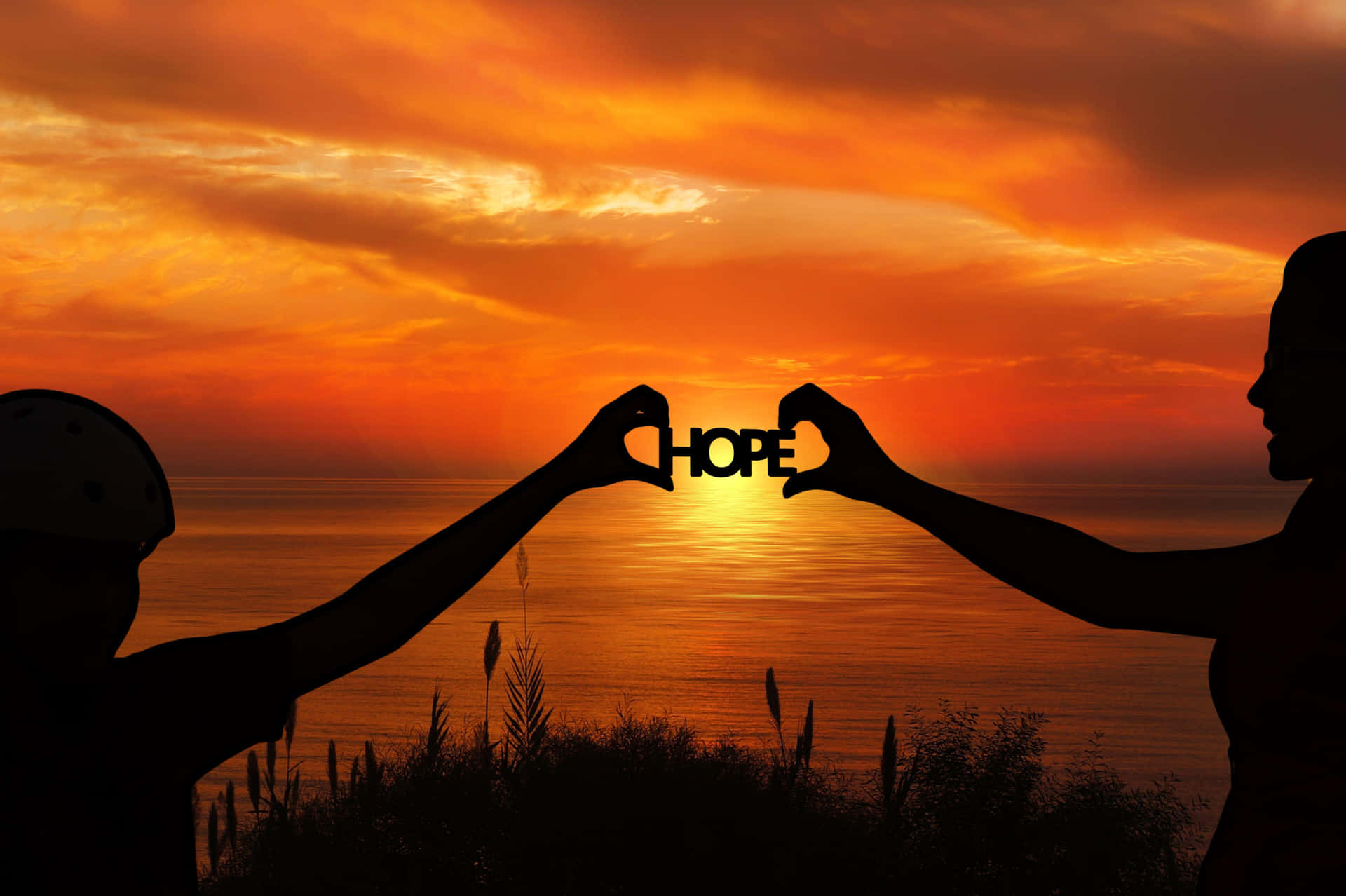 兩個人在日落時分以心形手勢托著「HOPE」一字。