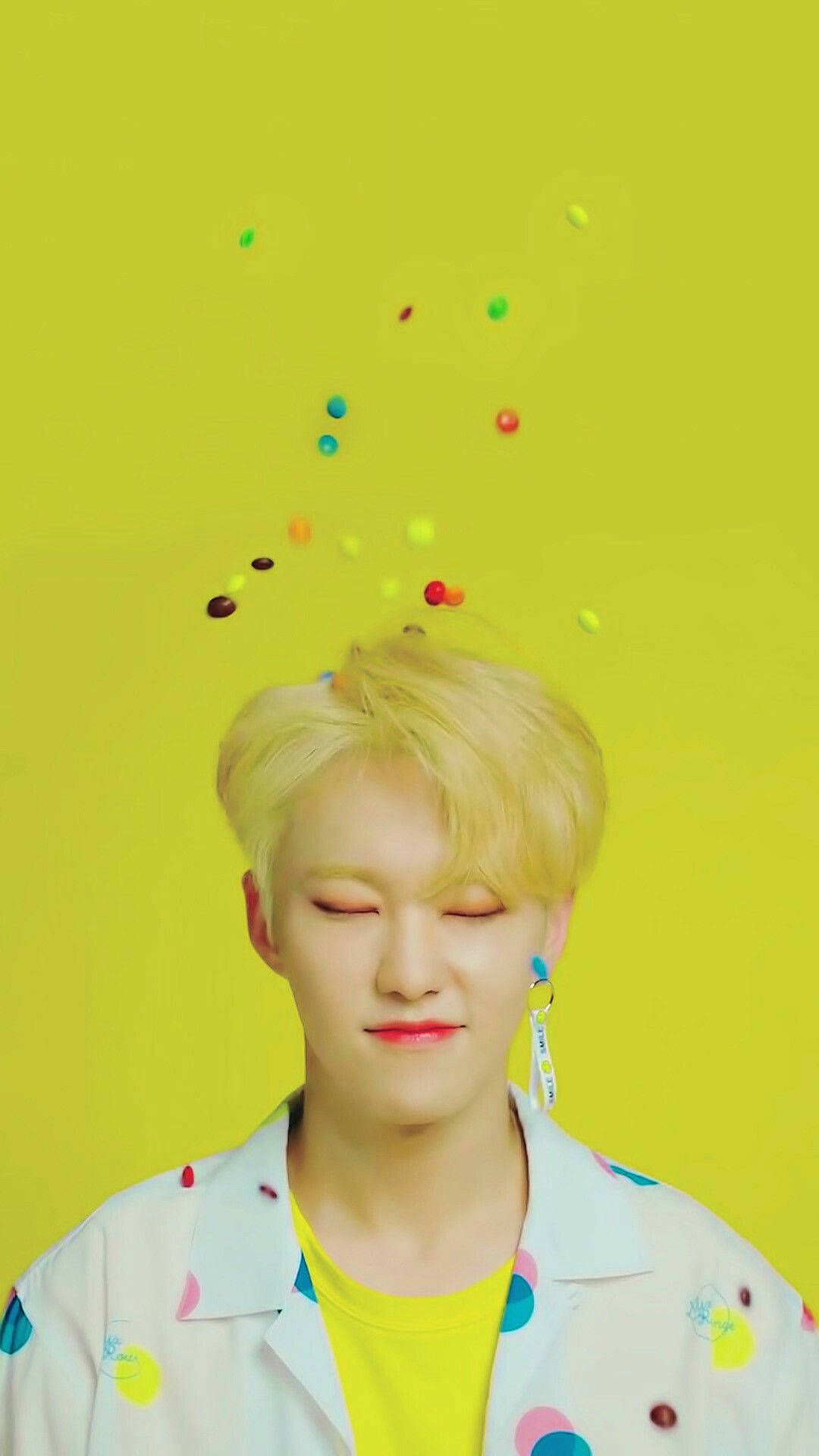 Hoshi 黃色風同人圖 壁紙 — 一個閉著眼睛、金髮的年輕男子在明亮的黃色背景前微笑，彩色糖果漂浮在他的頭周圍。