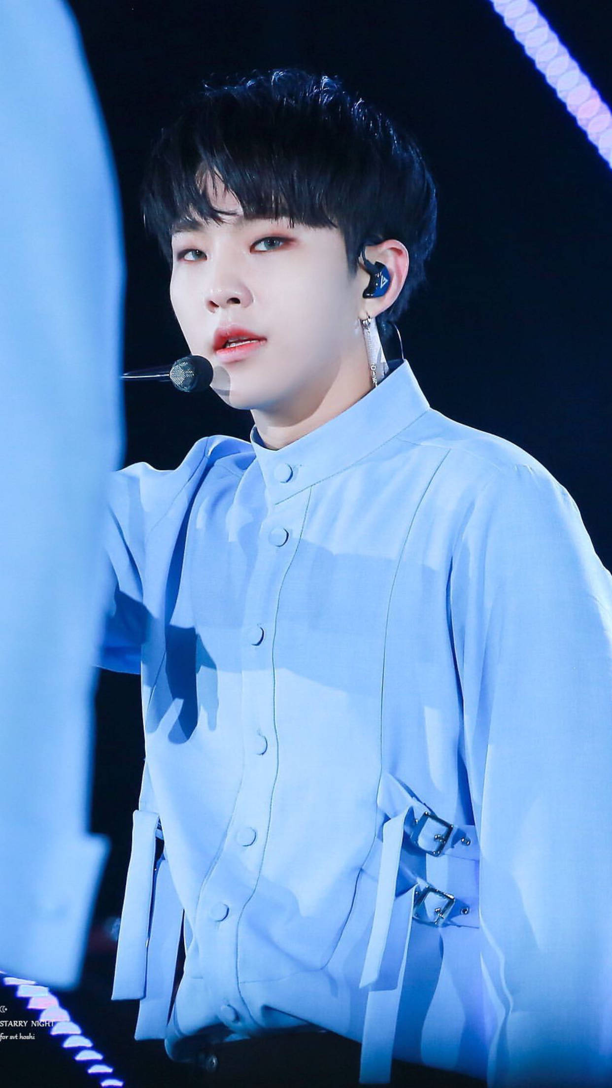 Hoshi 穿藍色服裝 壁紙 — 一位身穿淺藍色舞台服的年輕男表演者在明亮的藍色舞台燈光下對著麥克風唱歌。