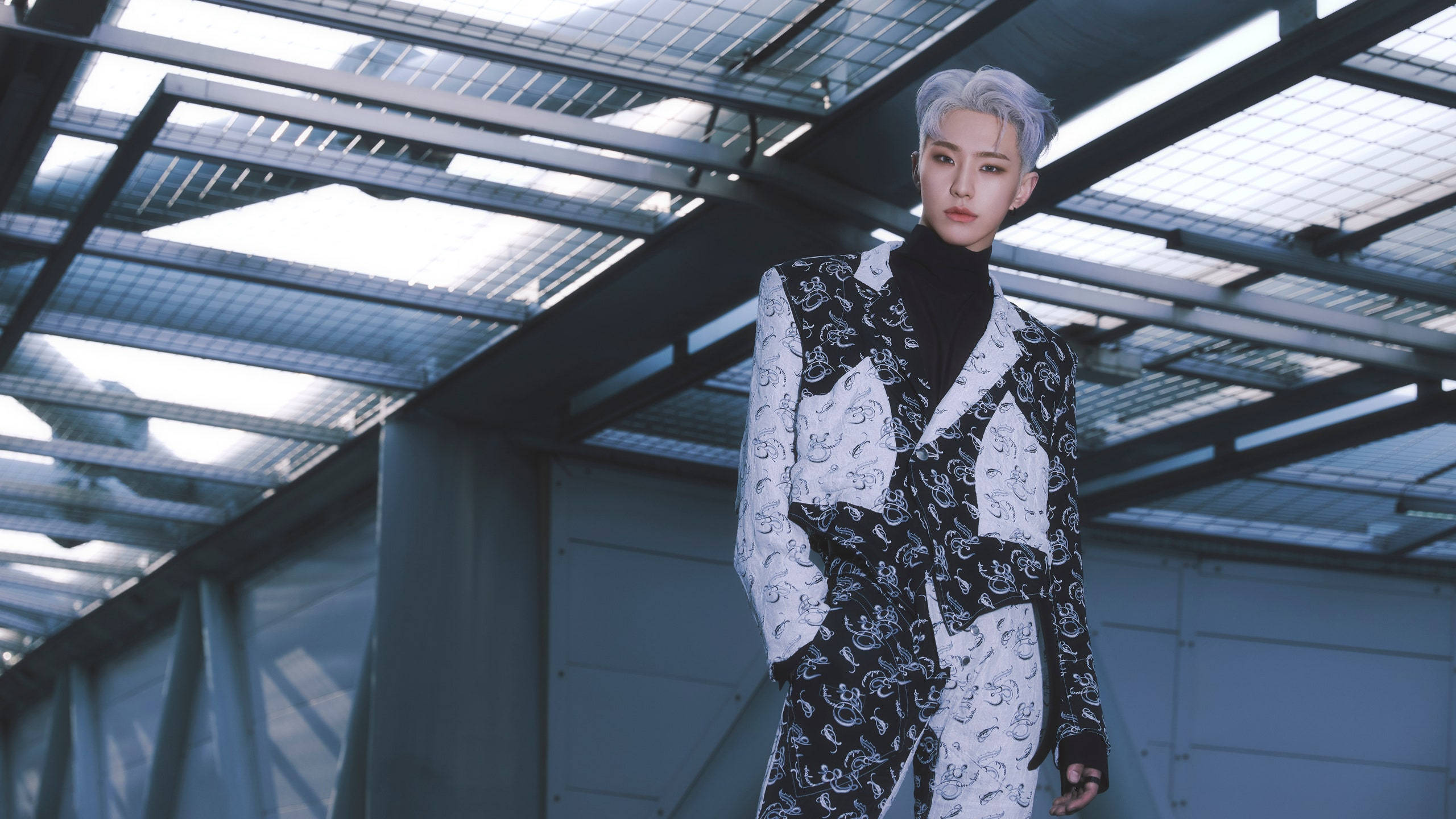 Hoshi SEVENTEEN 成員 壁紙 — 一位銀髮人士自信地站在現代玻璃與鋼結構屋頂下，身穿大膽的黑白圖案西裝。