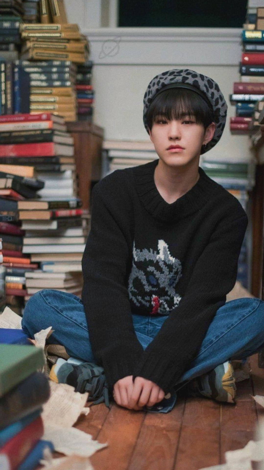 Hoshi 戴貝雷帽 壁紙 — 一位戴著豹紋貝雷帽和黑色毛衣的年輕人，在舒適的圖書館中盤腿坐在高聳的書堆之間。