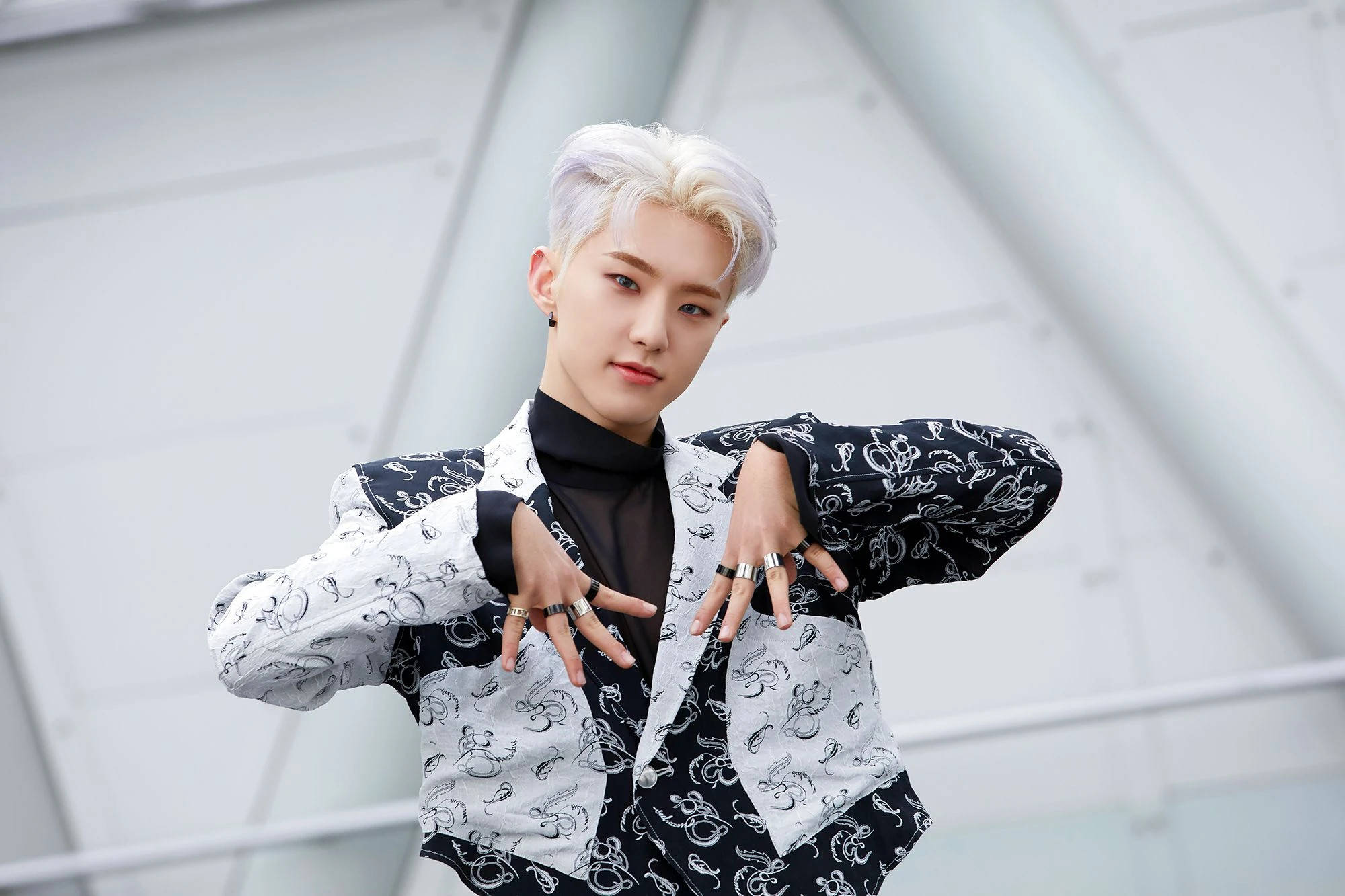 Hoshi 白髮風采 壁紙 — 一位時尚的年輕男子，留著鉑金色頭髮，穿著黑白圖案西裝外套，在現代白色建築背景下自信地擺出姿勢。