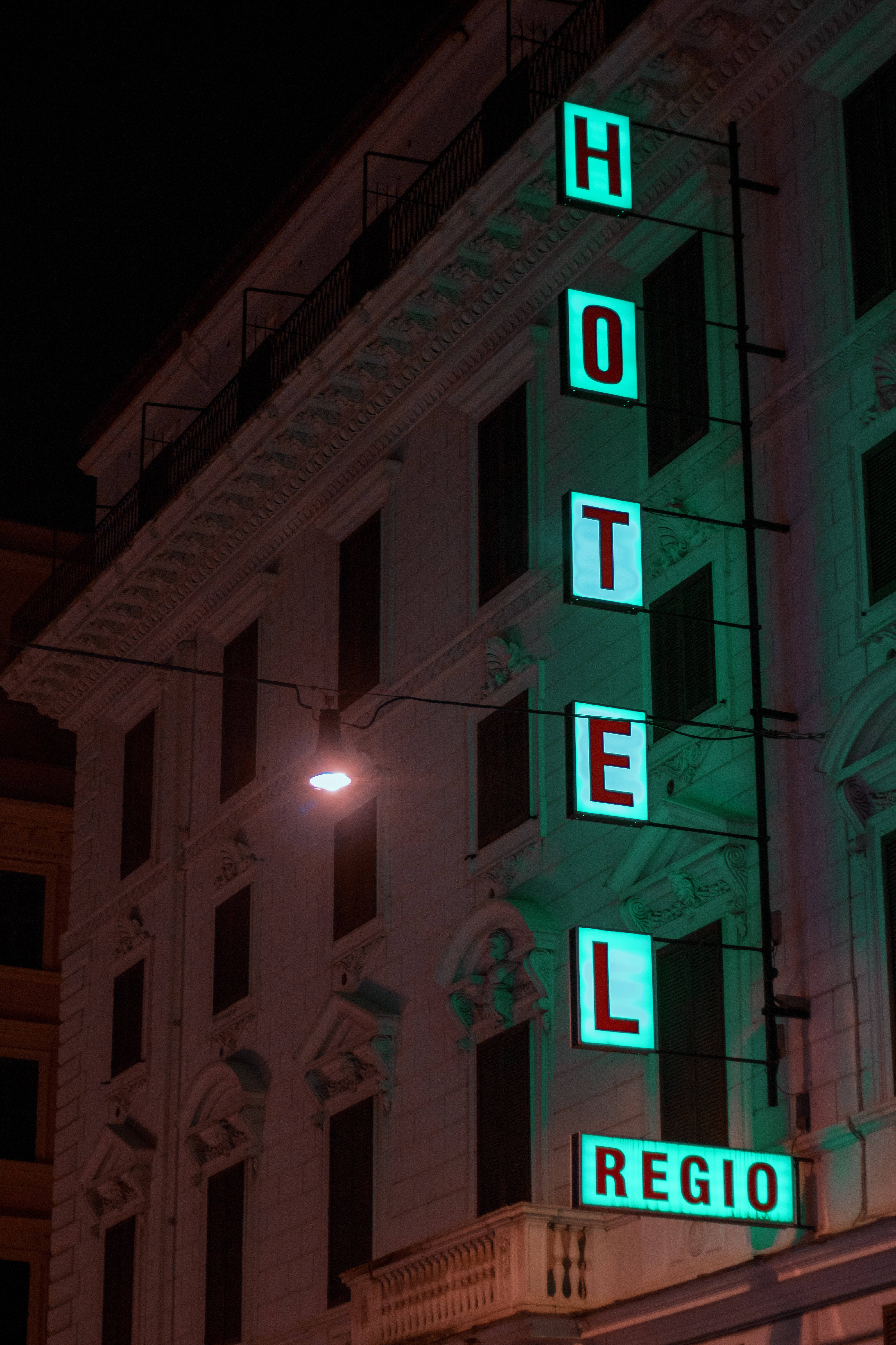 Hotel Regio 酒店招牌 壁紙 — 一棟復古酒店建築在夜晚被發光的綠色霓虹燈招牌照亮，招牌上拼寫著「HOTEL REGIO」，背景是黑暗的天空。