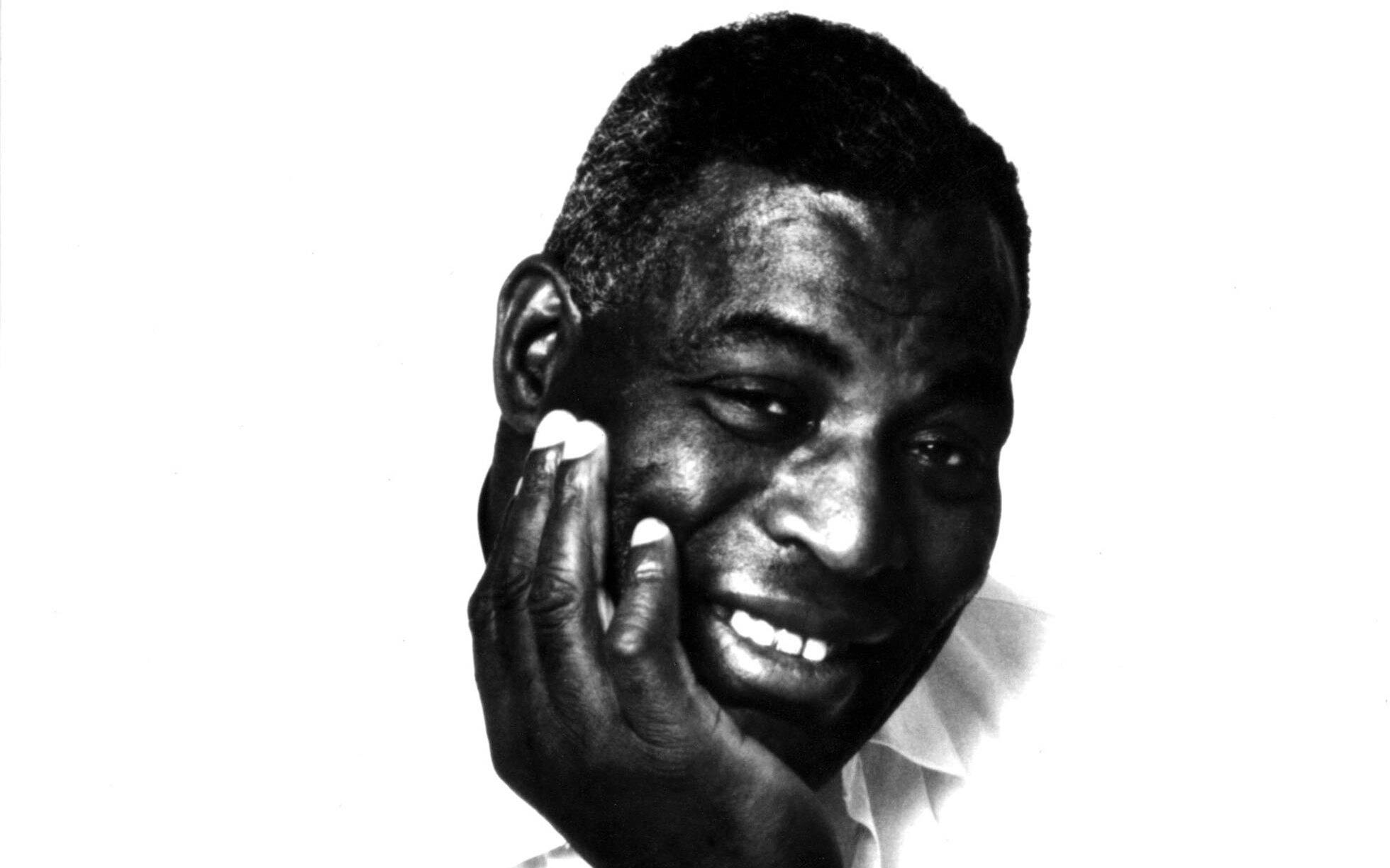 Howlin' Wolf 微笑演唱者照片 壁紙 — 一個快樂的黑白肖像，一個微笑的男人用手輕輕觸摸他的臉頰。
