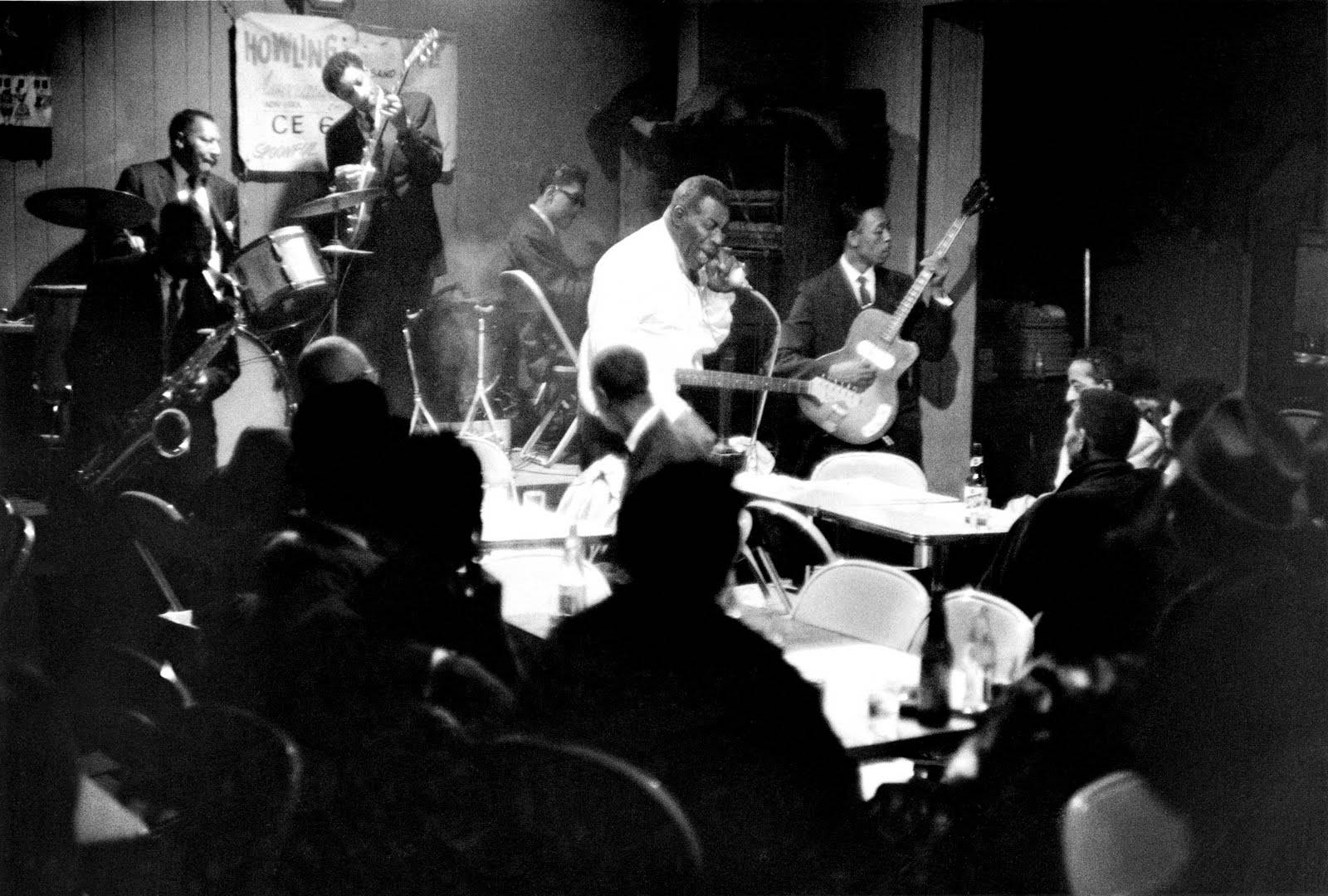 Howlin' Wolf 演出海報照片 壁紙 — 一張黑白照片捕捉到一個現場爵士樂隊在燈光昏暗的舞台上表演，前景有觀眾坐在桌子旁。