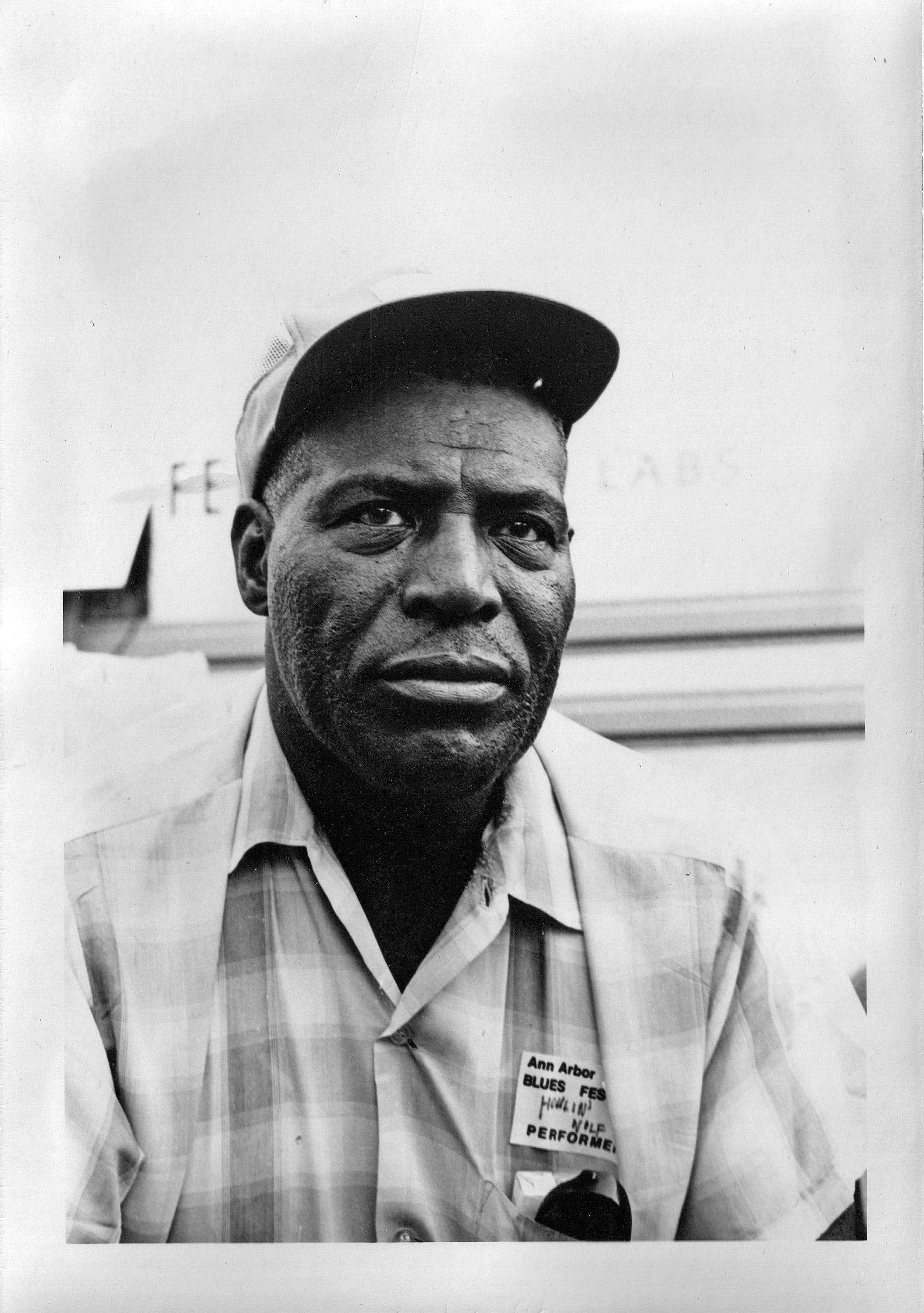 Howlin' Wolf 藍調歌手與吉他手照片 壁紙 — 一個黑白肖像，一名黑人男子戴著帽子、穿著格仔恤衫，在藍調音樂節上佩戴表演者徽章。