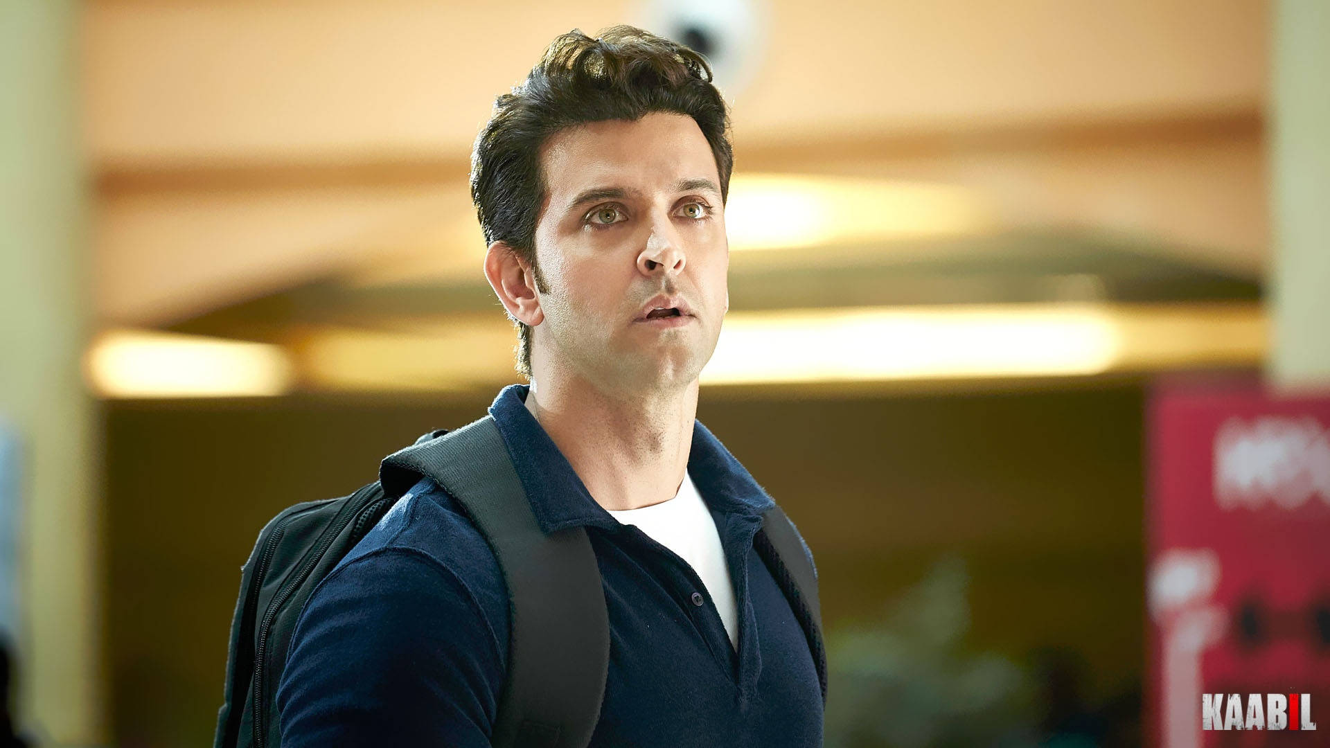 Hrithik Roshan《Kaabil》電影海報 壁紙 — 一名背著背包的男子在溫暖光線的室內空間中顯得驚訝。