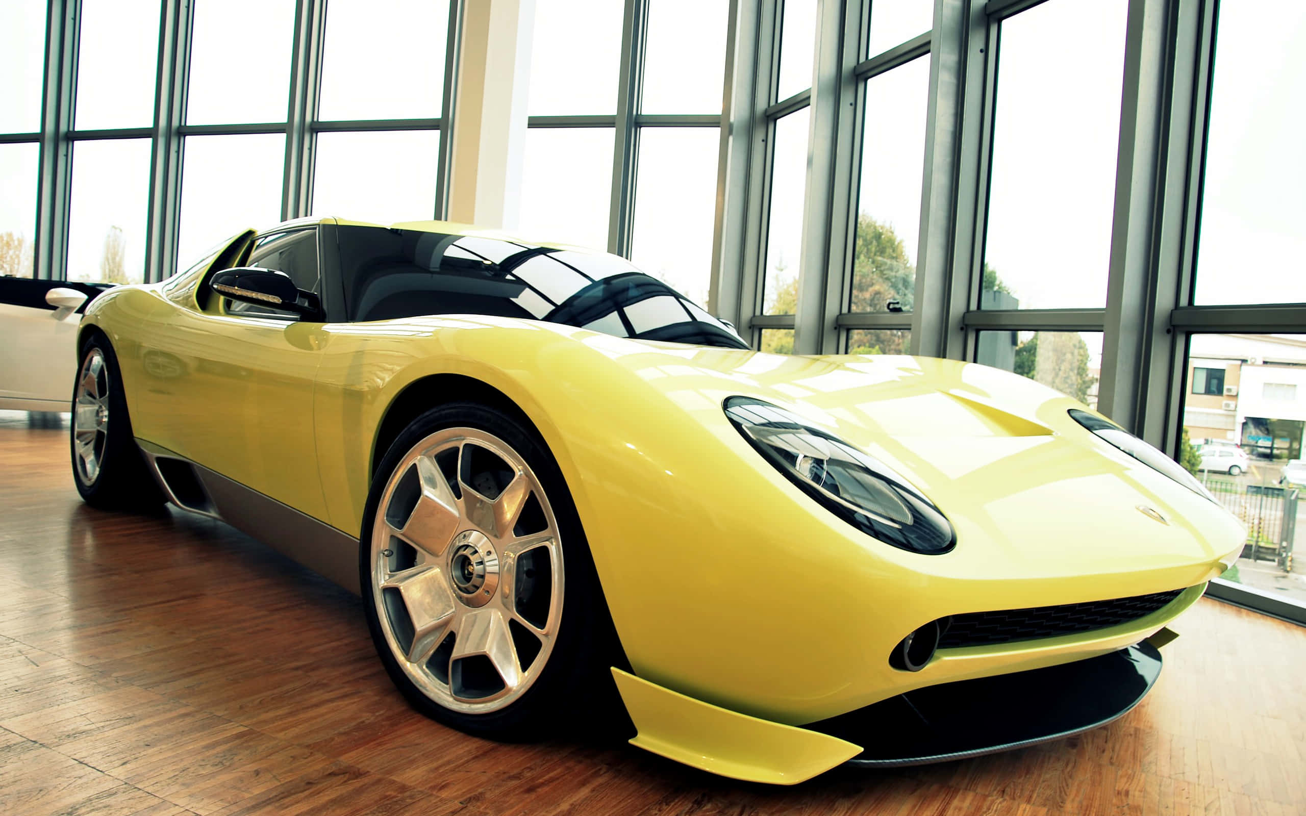 Lamborghini Miura 桌布 壁紙 — 一輛充滿活力的黃色跑車在自然光下，於現代玻璃牆展廳內閃閃發光，地板為木質。