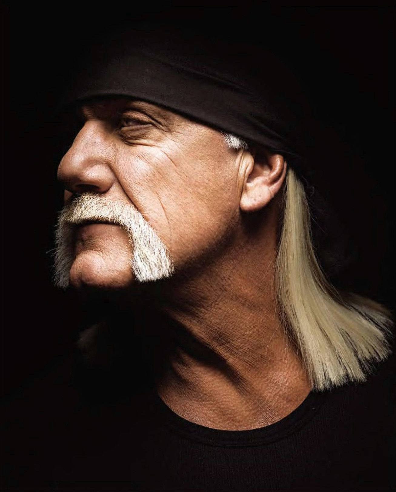 Hulk Hogan 獨照攝影 壁紙 — 一個戲劇性的肖像，一個留著白色山羊鬍和長金髮的男人，戴著黑色頭帶，背景是深色。