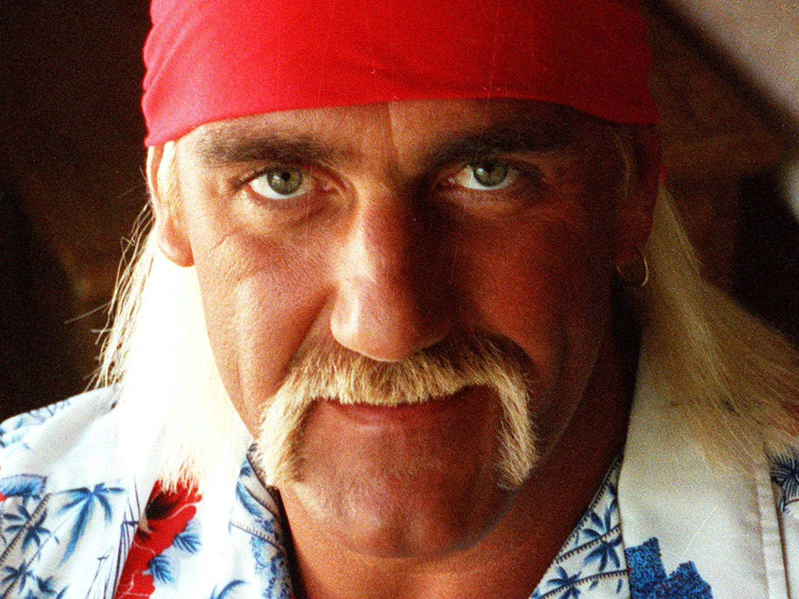 Hulk Hogan 經典馬蹄鬍 壁紙 — 一名戴紅色頭巾、留鬍鬚、身穿熱帶襯衫的男士的特寫肖像。