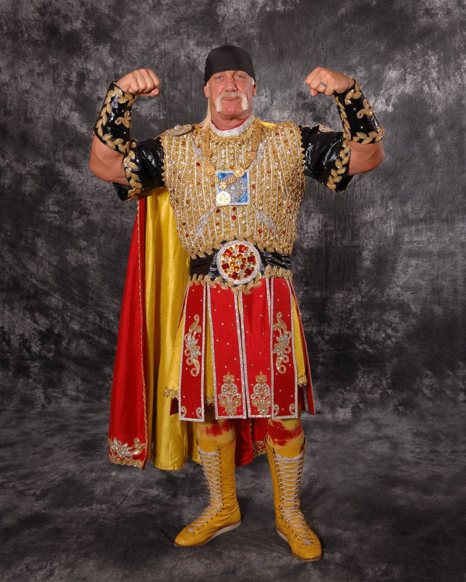 Hulk Hogan 華麗角鬥士裝束 壁紙 — Hulk Hogan 身穿金色和红色的角斗士服装，在深灰色工作室背景前展示肌肉。