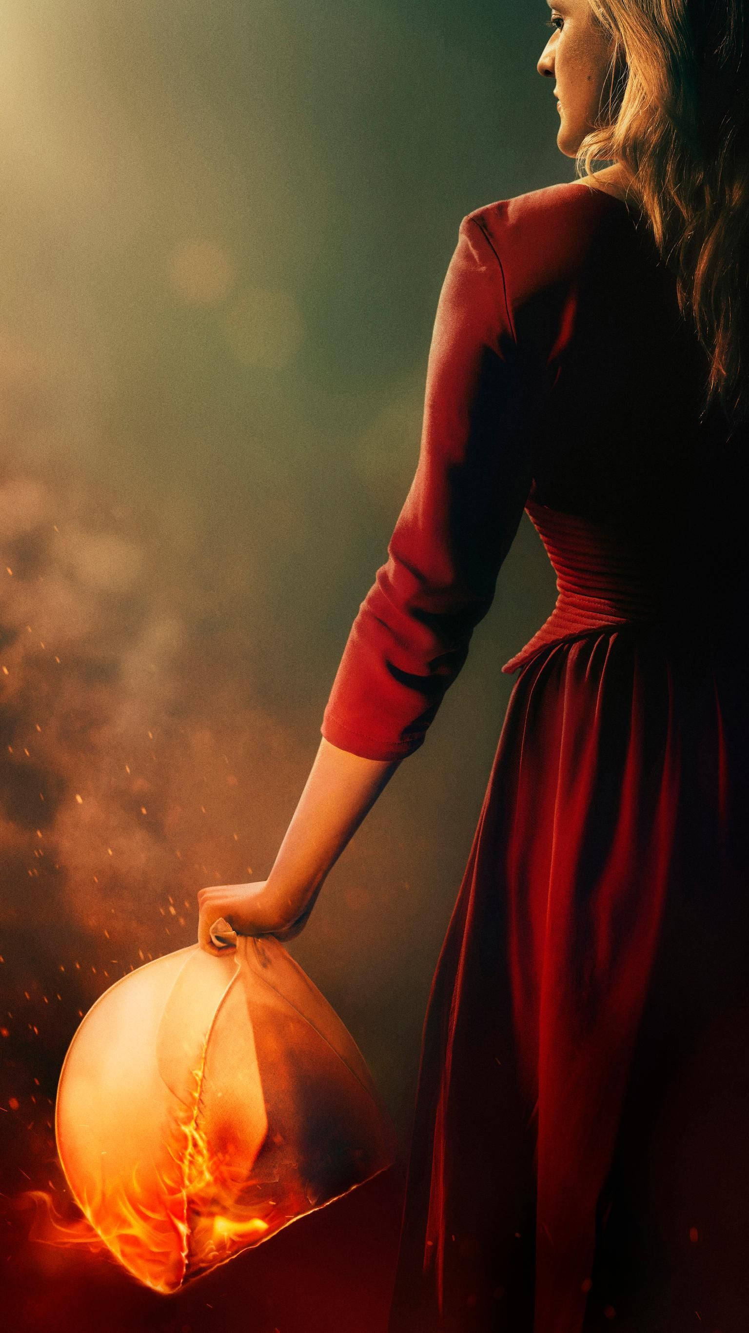 Hulu《使女的故事》劇照 壁紙 — 一位身穿紅色連衣裙的女性手持發光的燈籠，火焰在周圍舞動，場景充滿煙霧和溫暖的光線。