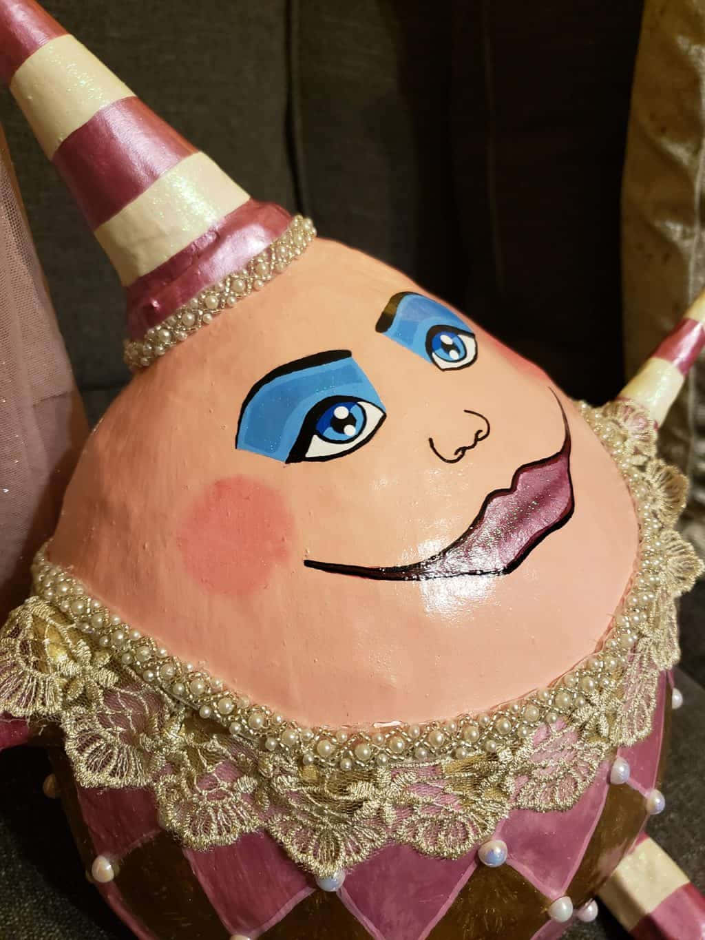 Humpty Dumpty 坐在牆上的經典插圖 壁紙 — 手繪陶瓷小丑頭，藍色眼睛，粉紅色臉頰，條紋帽子飾有金色蕾絲和珍珠。