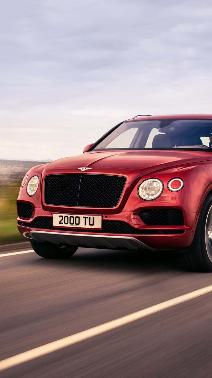 Bentley Bentayga 桌布 壁紙 — 一輛鮮紅色的賓利 Bentayga SUV 在柔和陰天下一條模糊的道路上飛馳。