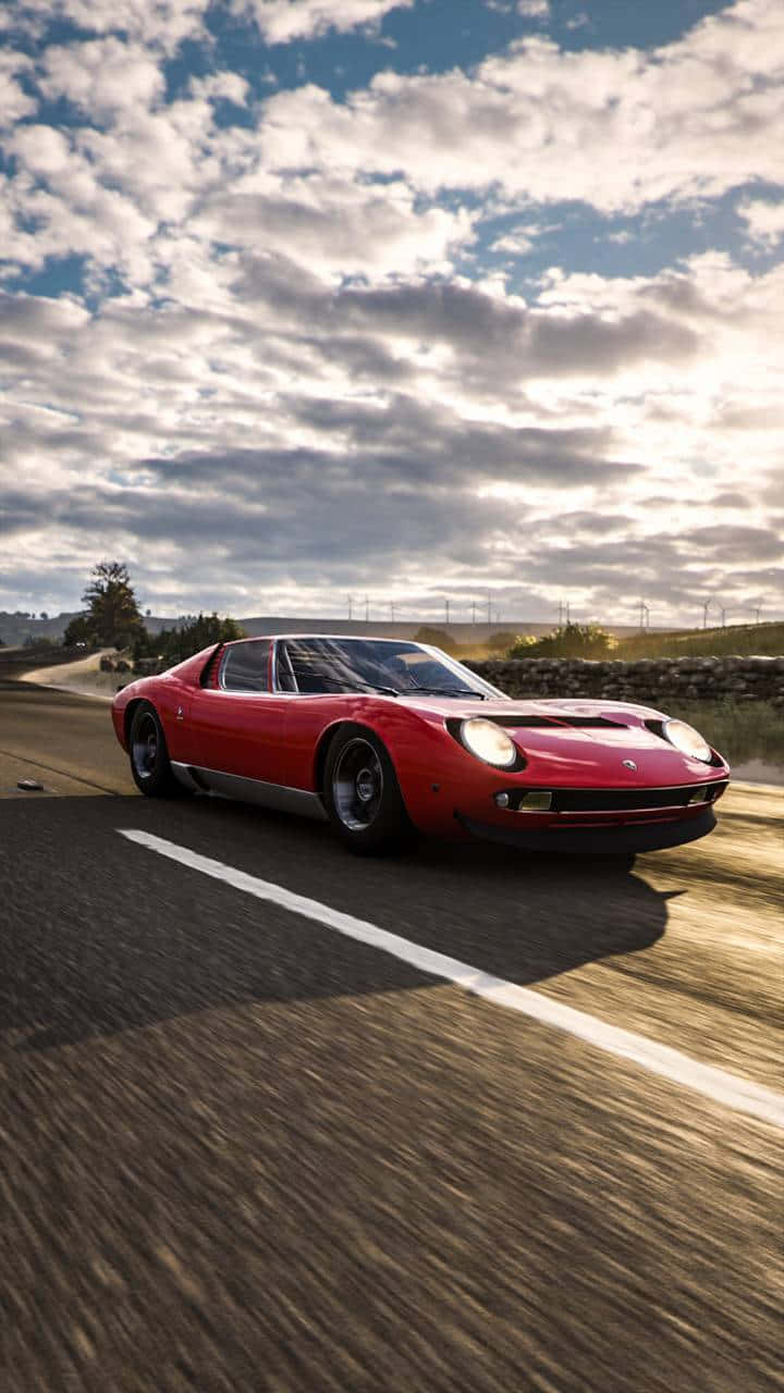 Lamborghini Miura 桌布 壁紙 — 一輛鮮紅色的經典跑車在戲劇性的多雲天空下，沿著蜿蜒的鄉村道路飛馳。