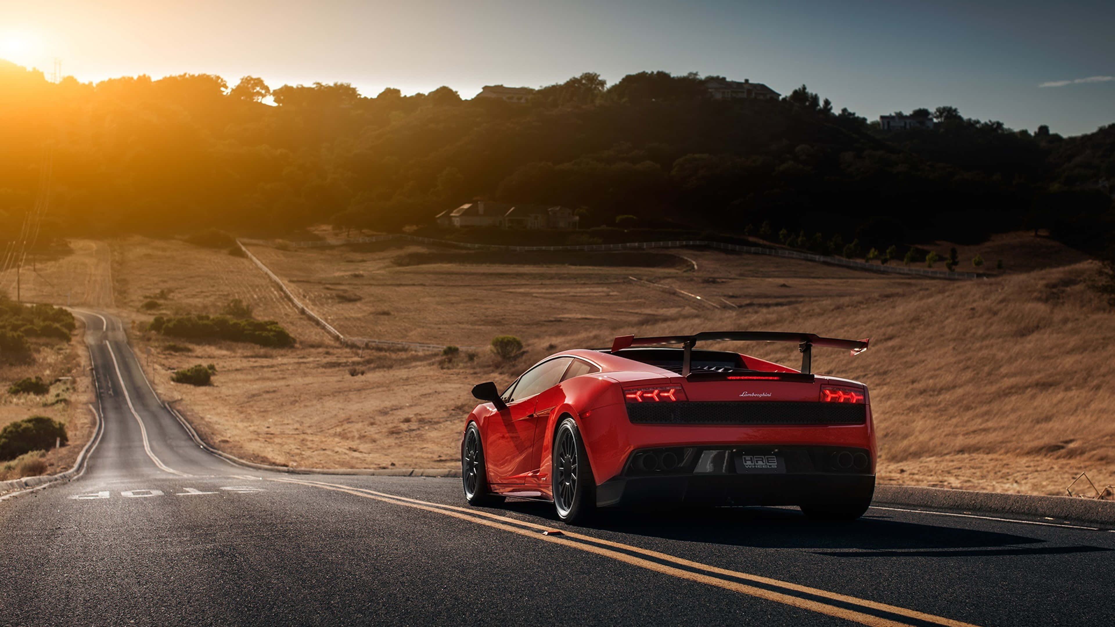 Lamborghini Gallardo 桌布 壁紙 — 一輛鮮紅色的林寶堅尼 Gallardo LP5702 Spyder 在金色日落時分沿著蜿蜒的瀝青道路行駛，背景是山丘。