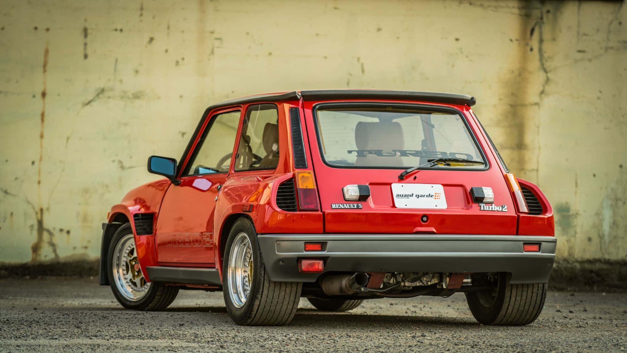 Renault 5 Turbo 桌布 壁紙 — 一輛鮮紅色的雷諾5 Turbo 2停泊在風化的混凝土牆前，展示其標誌性的尾部設計和運動姿態。