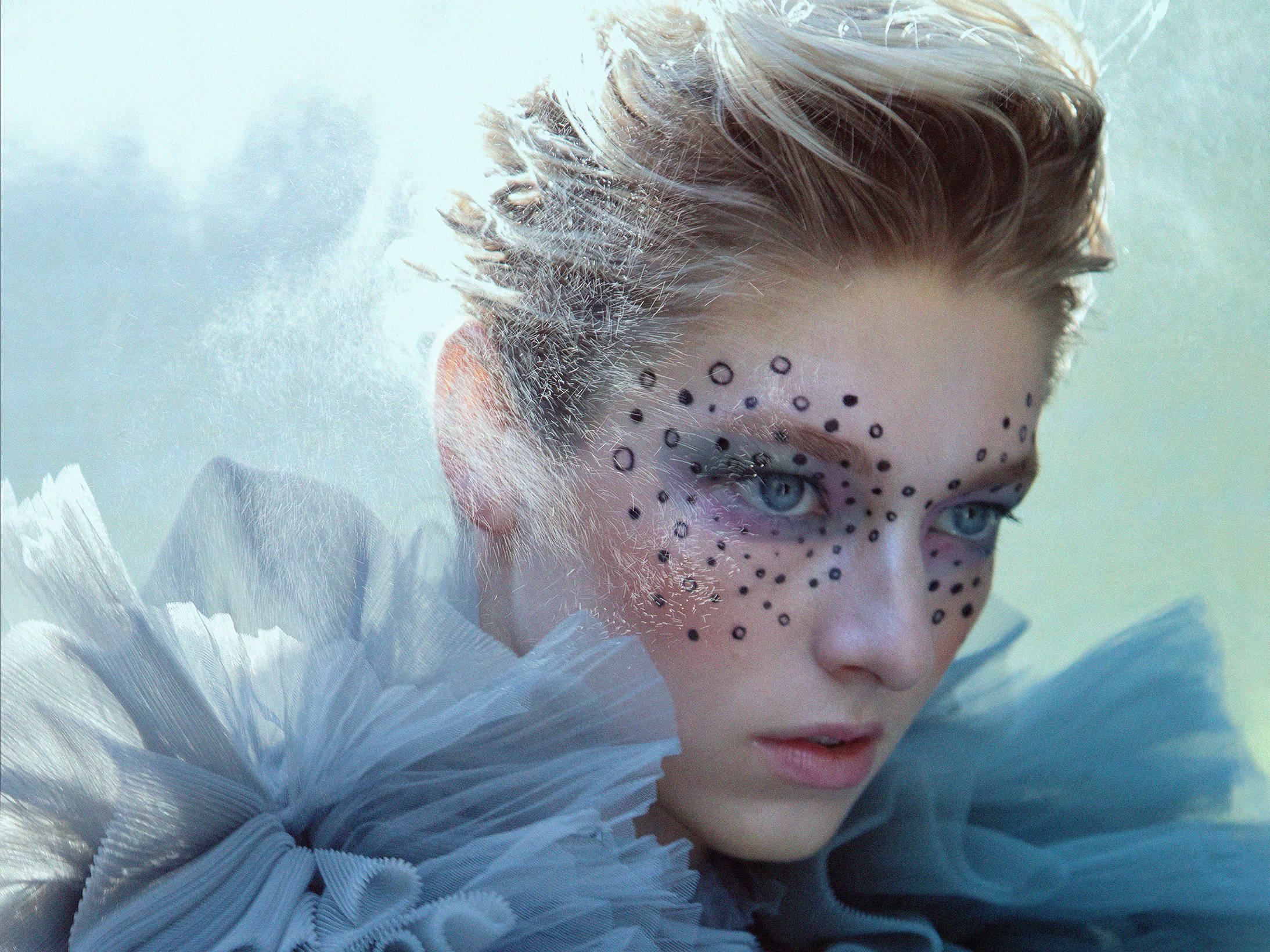 Hunter Schafer《Allure》雜誌拍攝 壁紙 — 一位擁有冰藍色眼睛和黑色圓點妝容的女性，穿著寬大的淡藍色荷葉邊領，透過薄霧凝視。