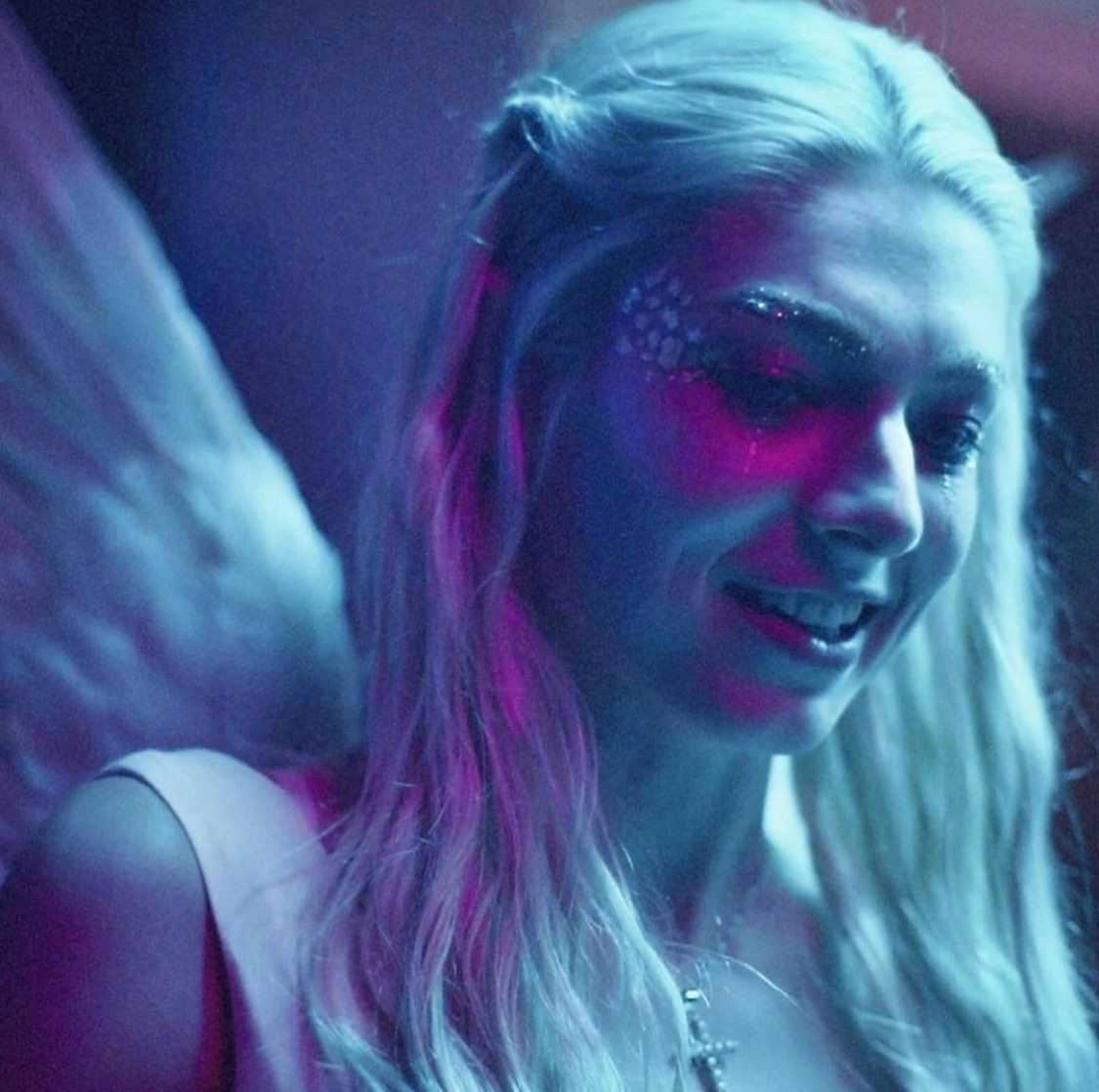 Hunter Schafer Jules 近照 壁紙 — 一位擁有發光翅膀和閃亮臉部彩繪的女性在霓虹紫和藍色燈光下微笑。
