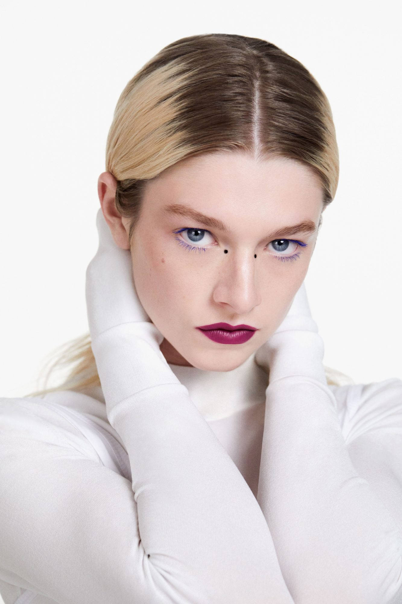 Hunter Schafer 激情造型 壁紙 — 一位金髮女子塗著大膽的紫色唇膏，戴著白色手套，在純白背景前凝視著。
