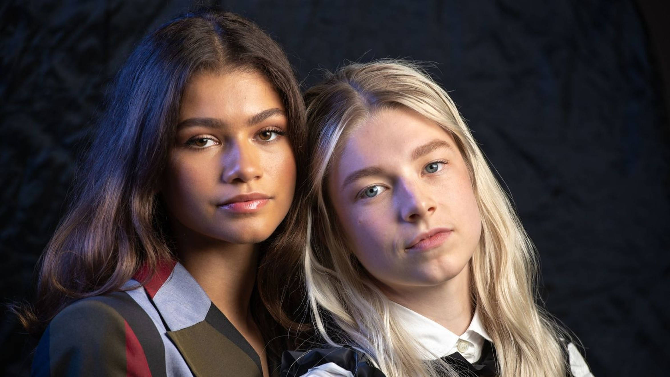 Hunter Schafer 與 Zendaya 壁紙 — 兩位髮色對比的年輕女性在深色紋理背景下直視鏡頭。