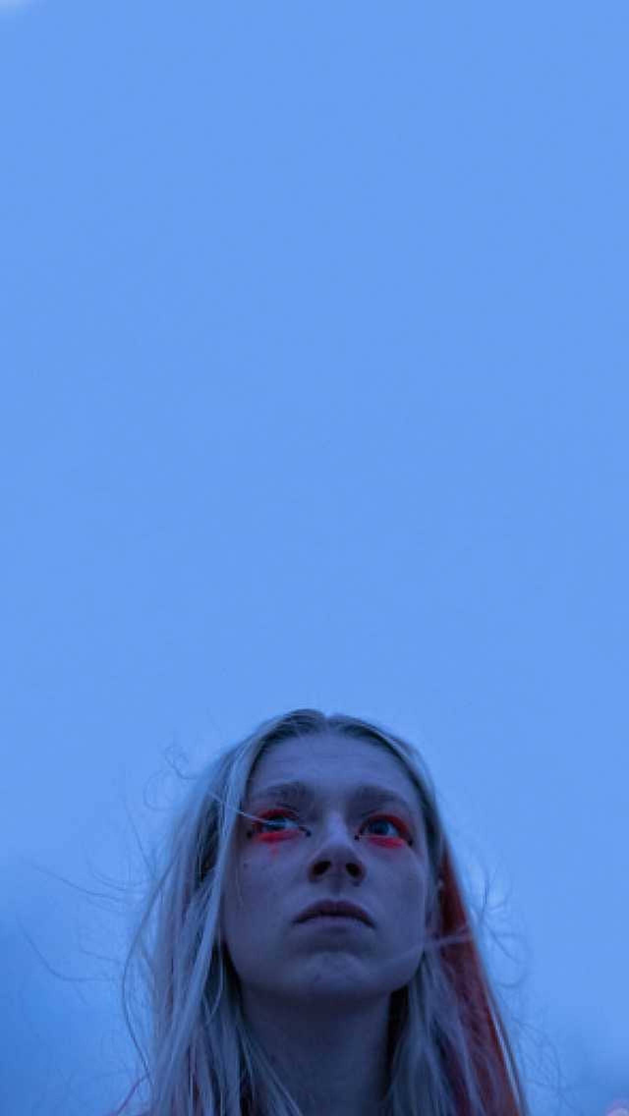 Hunter Schafer 藍色美學 壁紙 — 一個皮膚蒼白、眼睛紅色的人，仰望廣闊的藍天。