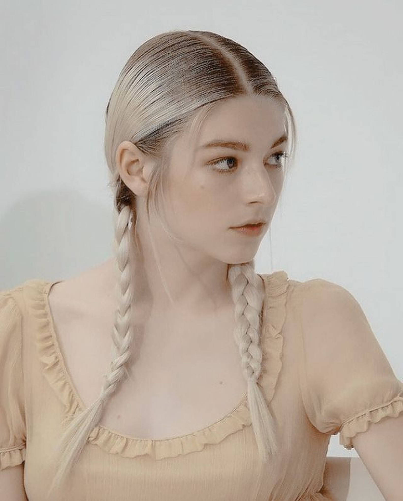 Hunter Schafer 鬢辮造型 壁紙 — 一位年輕女性，一頭鉑金色辮子，身穿柔軟米色荷葉邊上衣，背景為純白色。