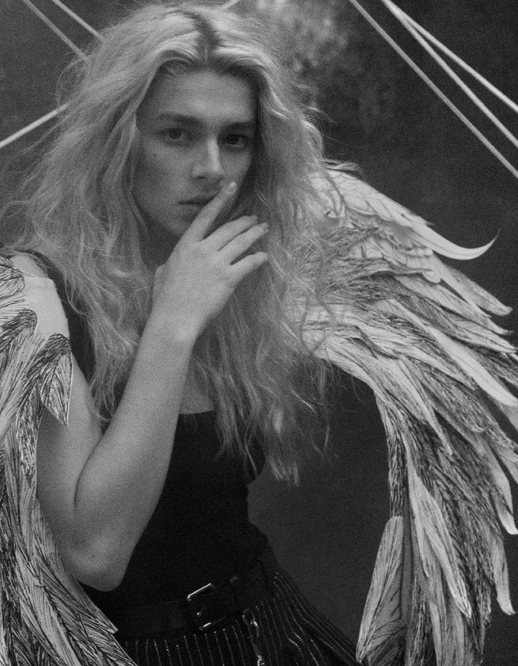 Hunter Schafer 黑白照 壁紙 — 一個人的單色肖像，長髮和詳細的羽毛翅膀，手靠近嘴，在幾何背景前。