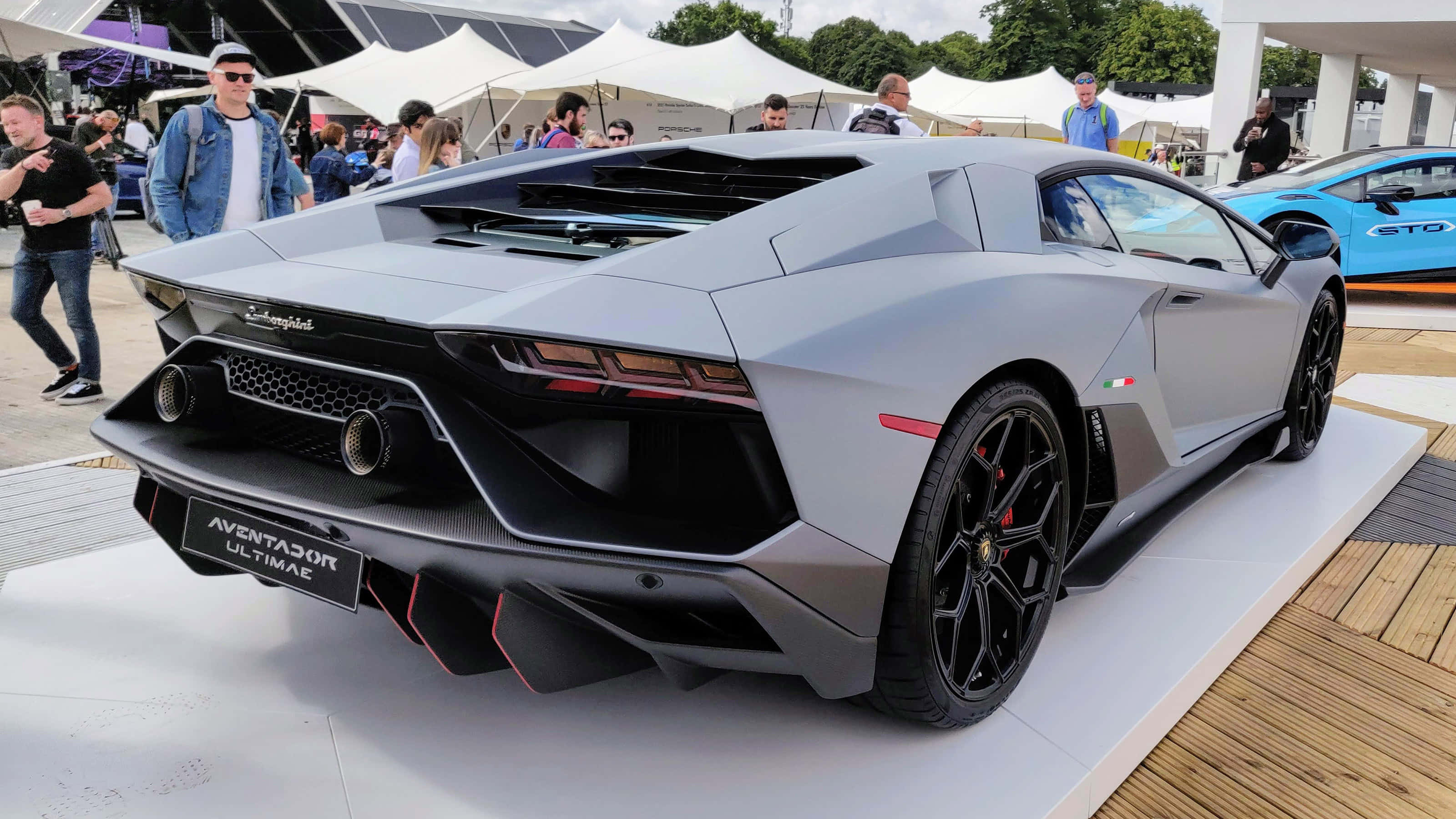 一輛蘭博基尼Huracán在車展上展出 壁紙 — 一輛時尚的銀色林寶堅尼Aventador Ultimae在戶外車展上展出，背景有人群和白色帳篷。