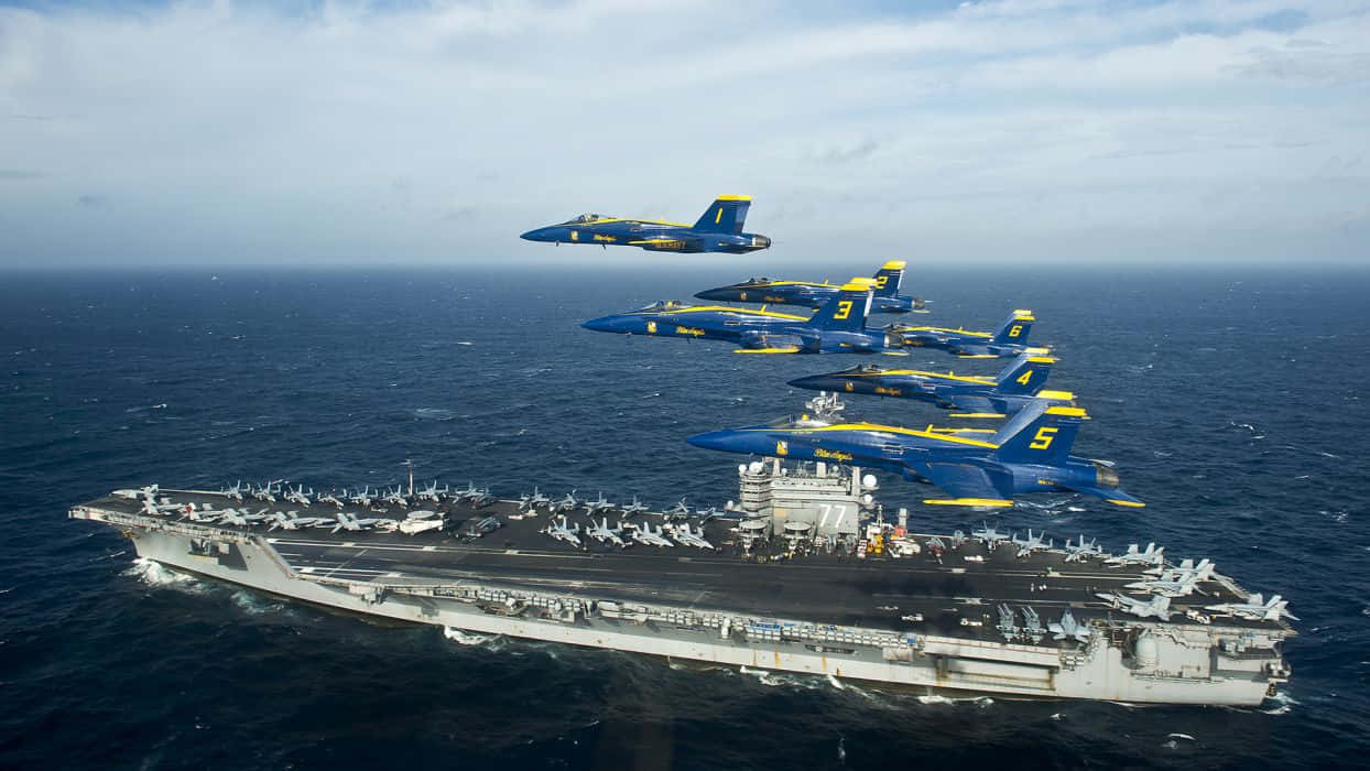 藍天使飛越「喬治·H·W·布希號」航空母艦 壁紙 — 藍色和黃色的戰鬥機在公海航行的大型航空母艦上空以緊密編隊飛行。