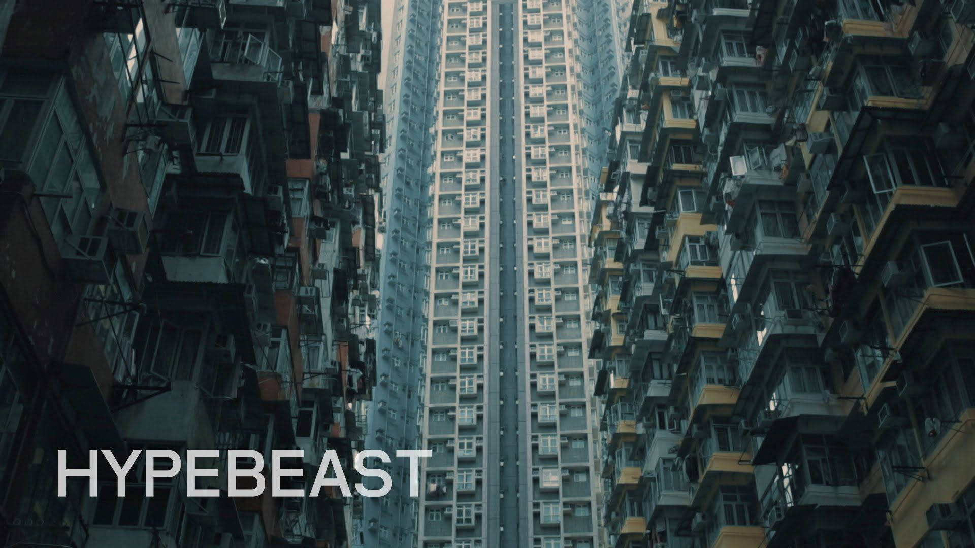 以Hypebeast視角欣賞城市風景 壁紙 — 狹窄的城市峽谷，由高聳的住宅建築構成，佈滿密集的陽台和空調機，天空暗淡。