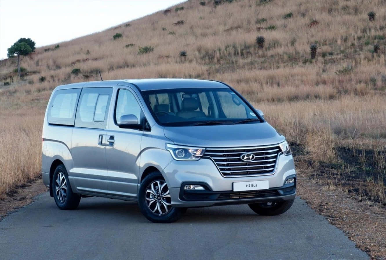 銀色現代HI Bus客貨車停泊在鄉村道路上，背景有乾草山丘。