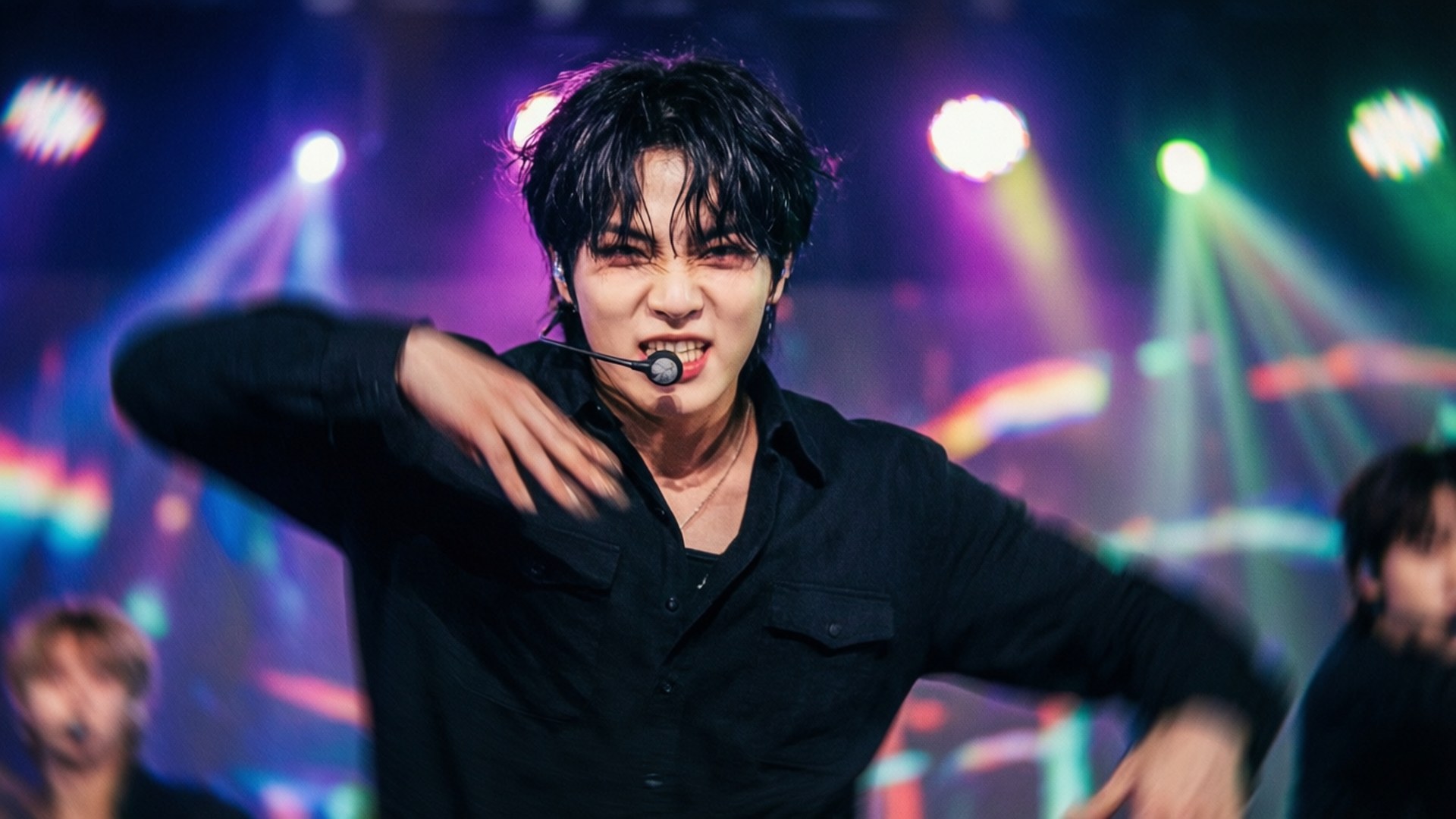 Hyunjin 舞動瞬間 壁紙 — 一位身穿黑色襯衫的男性表演者在充滿活力的紫色、綠色和藍色舞台燈光下，戴著麥克風耳機激烈地跳舞。