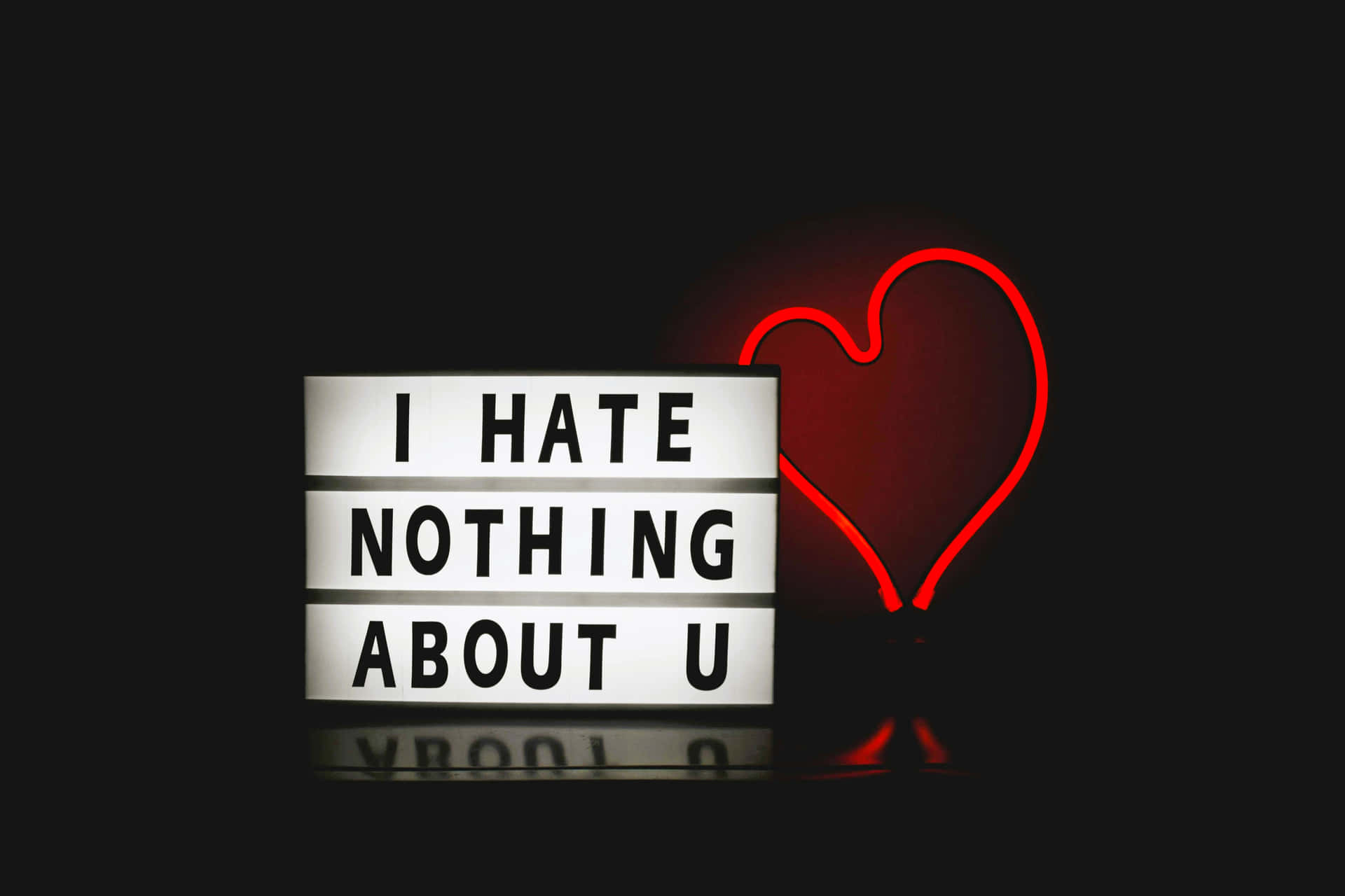 一個燈箱，上面有文字 I HATE NOTHING ABOUT U，旁邊有一個紅色霓虹心形，背景為黑色。