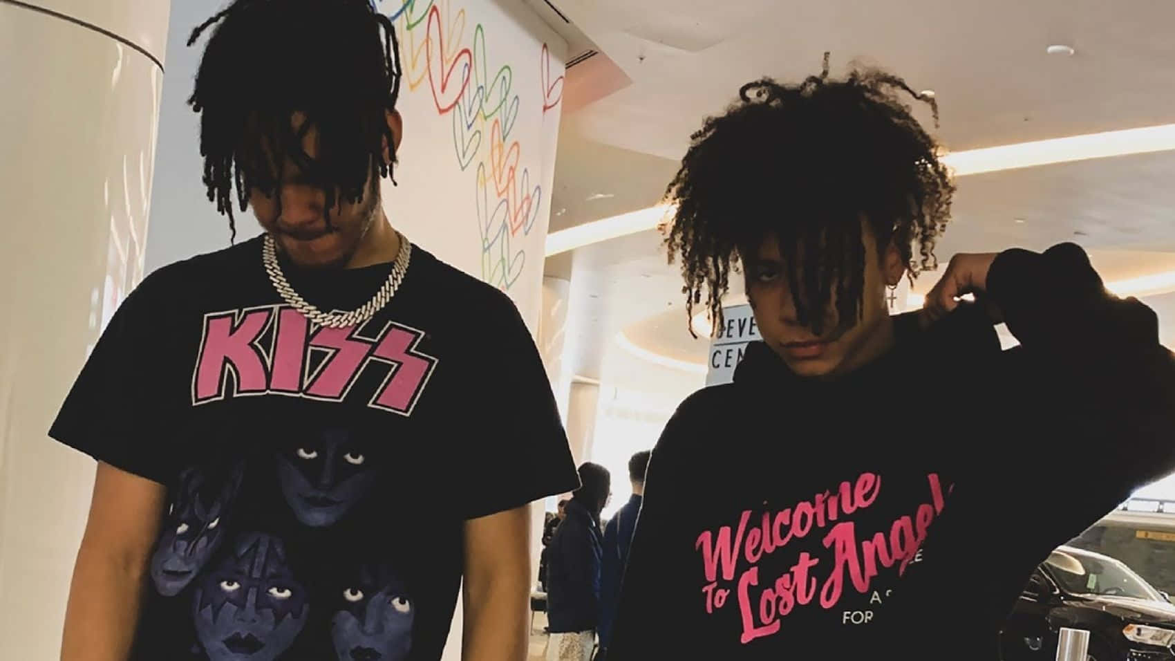 Iann Dior 與友合照 壁紙 — 兩名年輕男子留著辮子頭在室內擺姿勢，一人穿著Kiss T恤，另一人穿著Welcome to Lost Angeles連帽衫。
