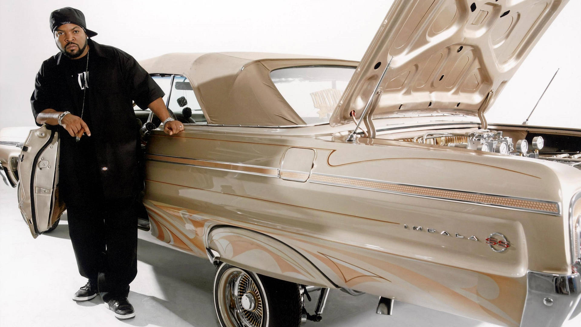 Ice Cube 男歌手與汽車 壁紙 — 一名身穿黑色衣服的男子自信地站在一輛打開引擎蓋、露出鍍鉻引擎部件的米色經典汽車旁。