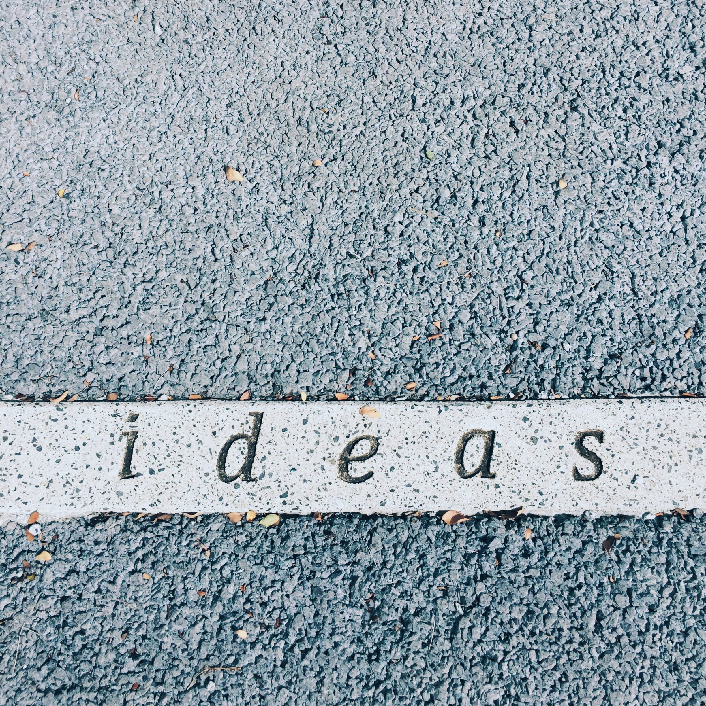 牆上「Ideas」字體 壁紙 — 混凝土路緣石的近距離特寫，上面刻有「想法」一詞，背景為有紋理的瀝青路面。