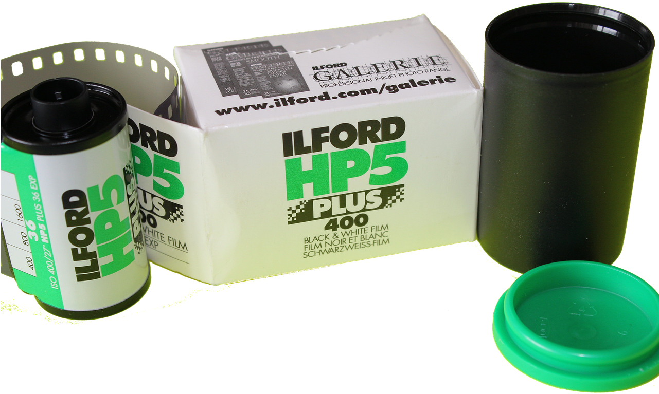 Ilford HP5 Plus 黑白膠片 壁紙 — 一個復古Ilford HP5 Plus 400黑白菲林罐連同其盒子和一個綠色菲林容器蓋子，放在純黑色背景前。