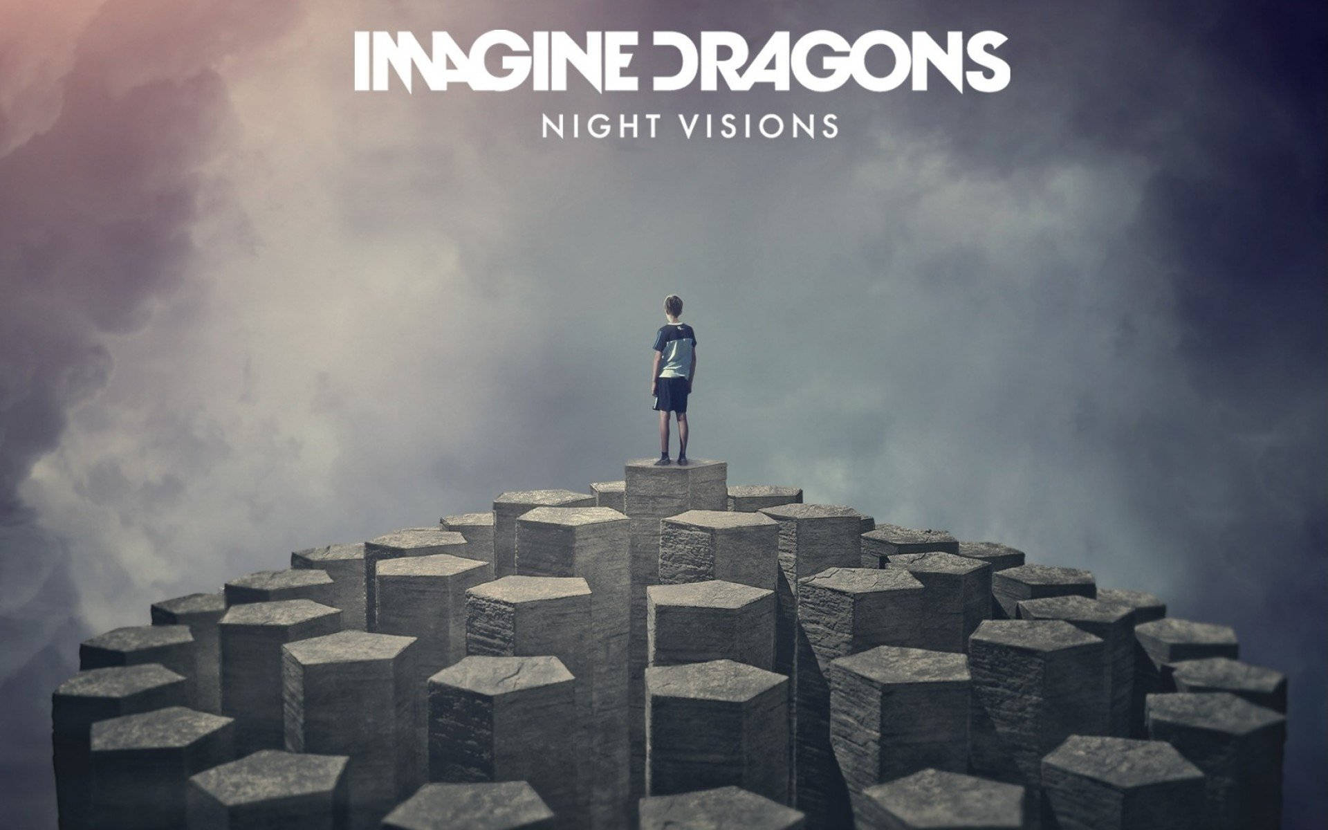 Imagine Dragons《Night Visions》專輯海報 壁紙 — 一個孤獨的身影站在石製六角形平台上，背景是戲劇性的多雲天空，並有文字疊加。