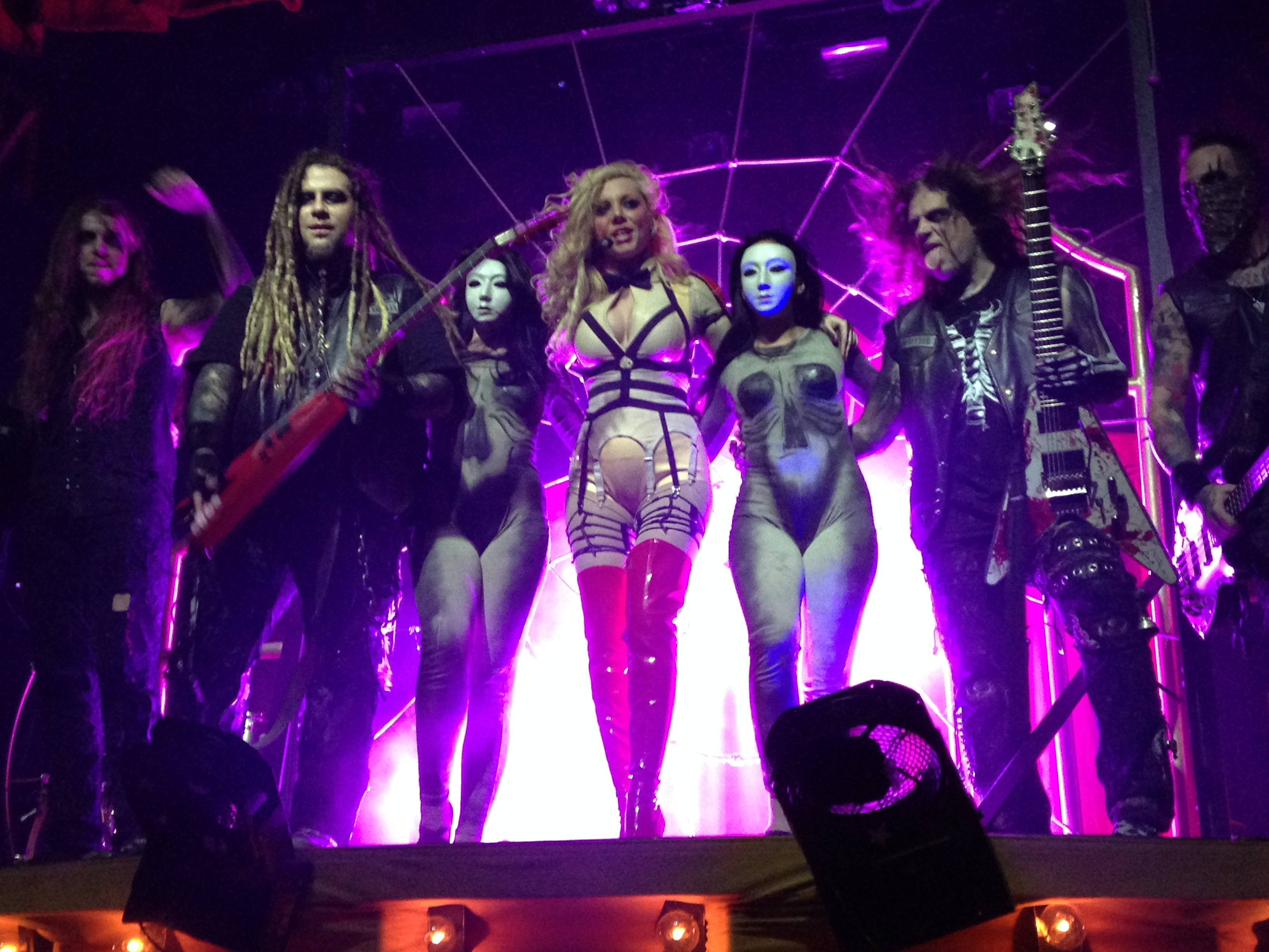 In This Moment《Black Widow》巡迴演出 壁紙 — 一支搖滾樂隊在充滿活力的紫色燈光下在舞台上表演，成員穿著暴露的服裝並拿著結他。